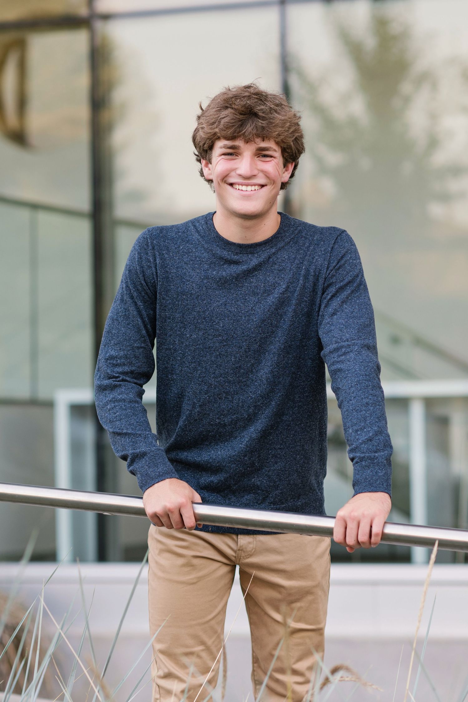 Young person in navy sweater smiles while leaning on railing outdoors.
