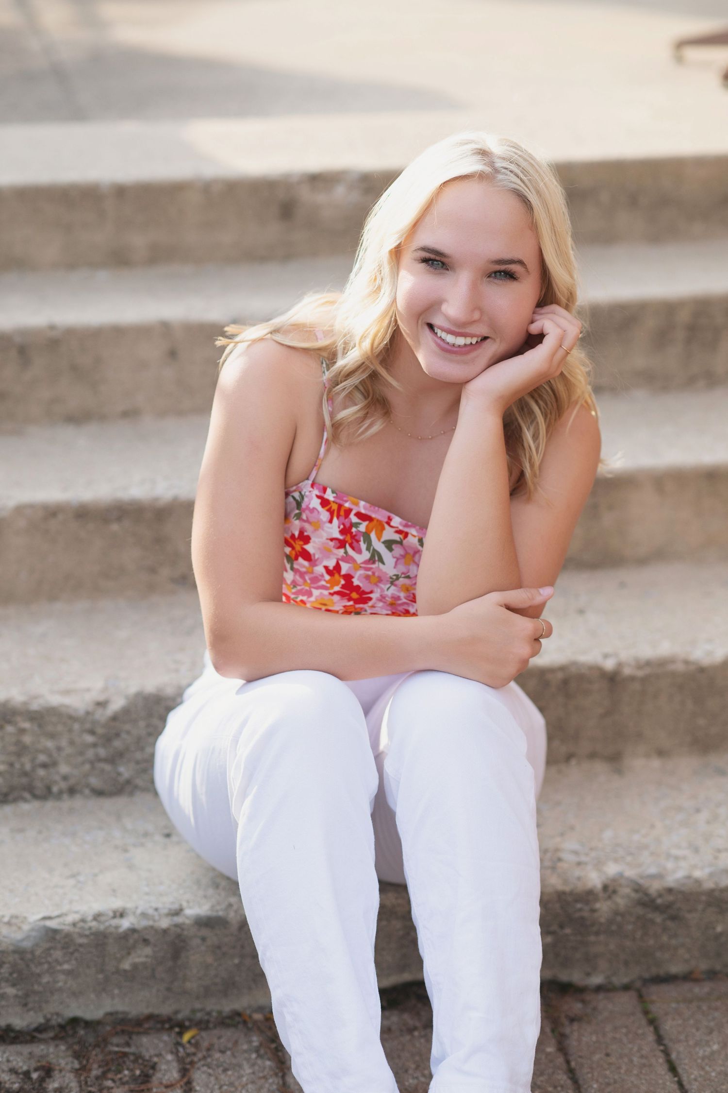 A person wearing a floral top and white pants sits casually on concrete steps outdoors.