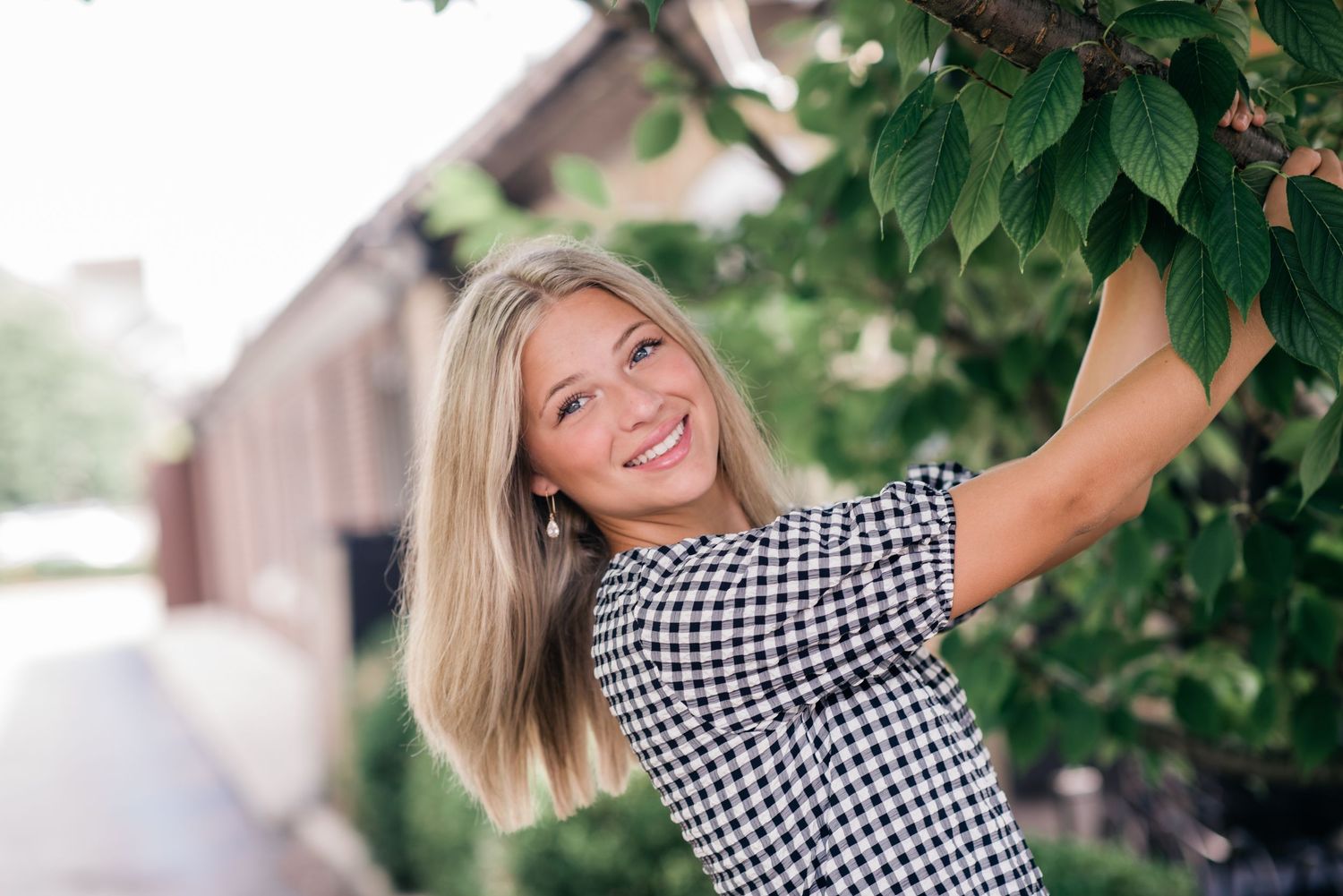Dublin Ohio Senior portrait in gingham dress poses joyfully under green foliage in outdoor photoshoot.