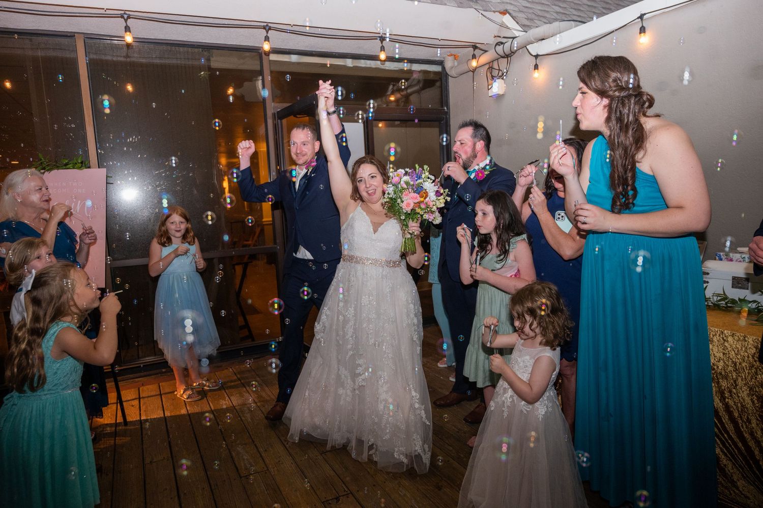 Wedding reception dance floor filled with guests in formal attire and teal bridesmaid dresses.