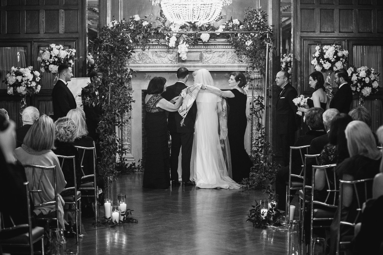 Wedding ceremony in a grand hall with floral arrangements lining the aisle.