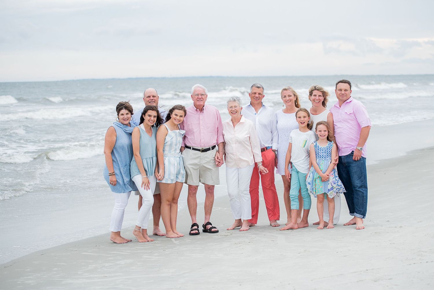 Hilton Head generation photo coordinating pastel outfits poses together on a sunny beach with ocean waves in the background.