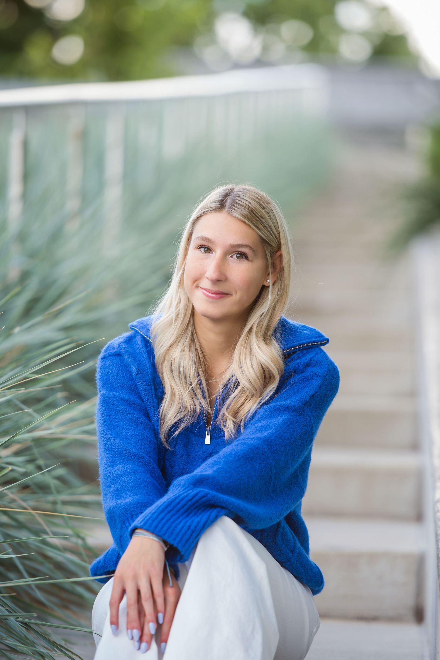 Person in bright blue sweater and white dress poses thoughtfully against natural background.