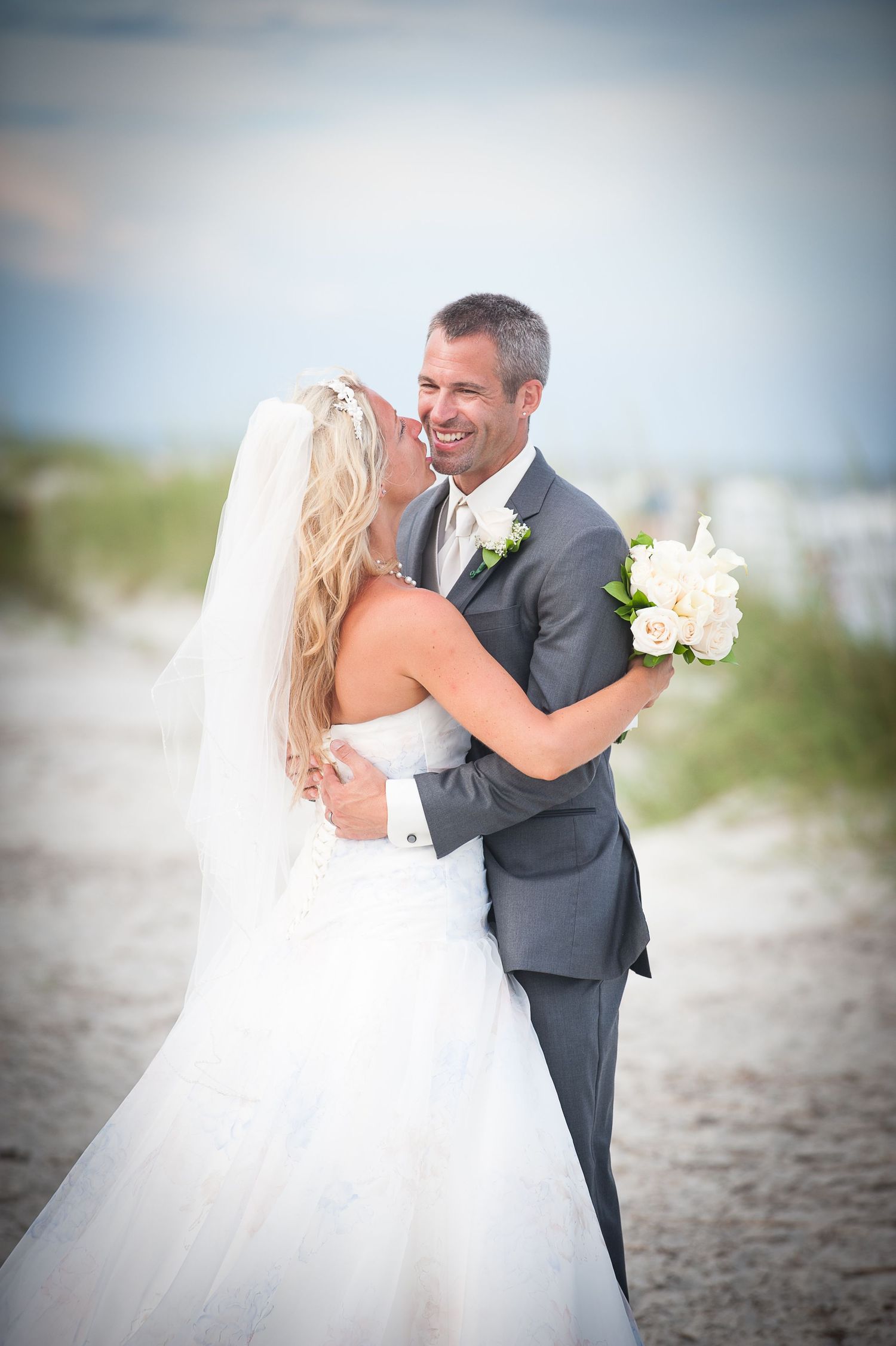 A joyful Hilton Head couple embraces on a beach during their wedding ceremony, with the bride holding a white bouquet.