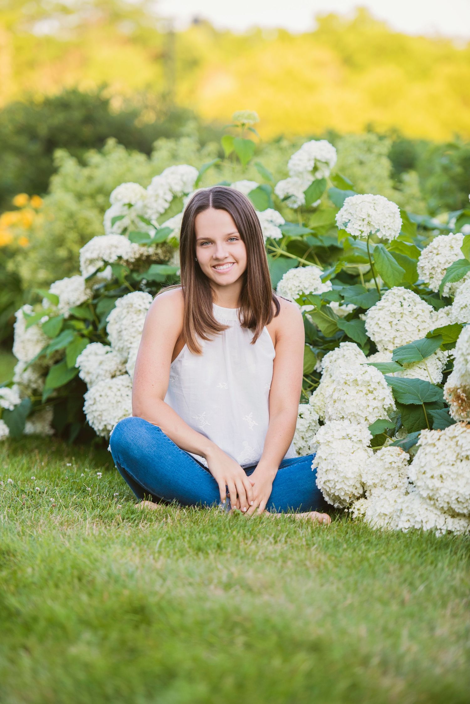 Outdoor portrait session in a garden with blooming white hydrangea bushes and lush green grass on a sunny summer day.
