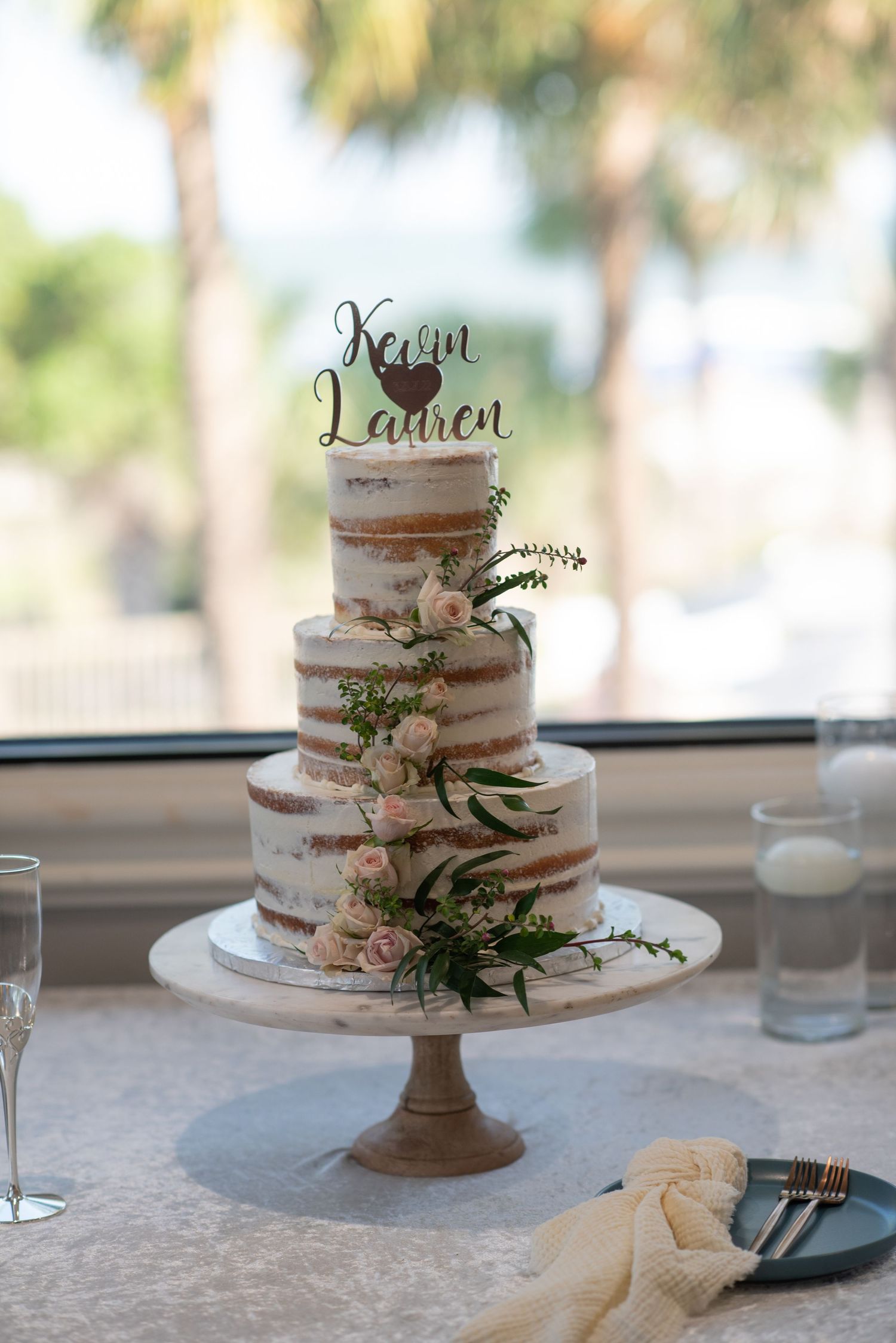Elegant three-tiered naked wedding cake decorated with fresh flowers and greenery on display. Hilton Head