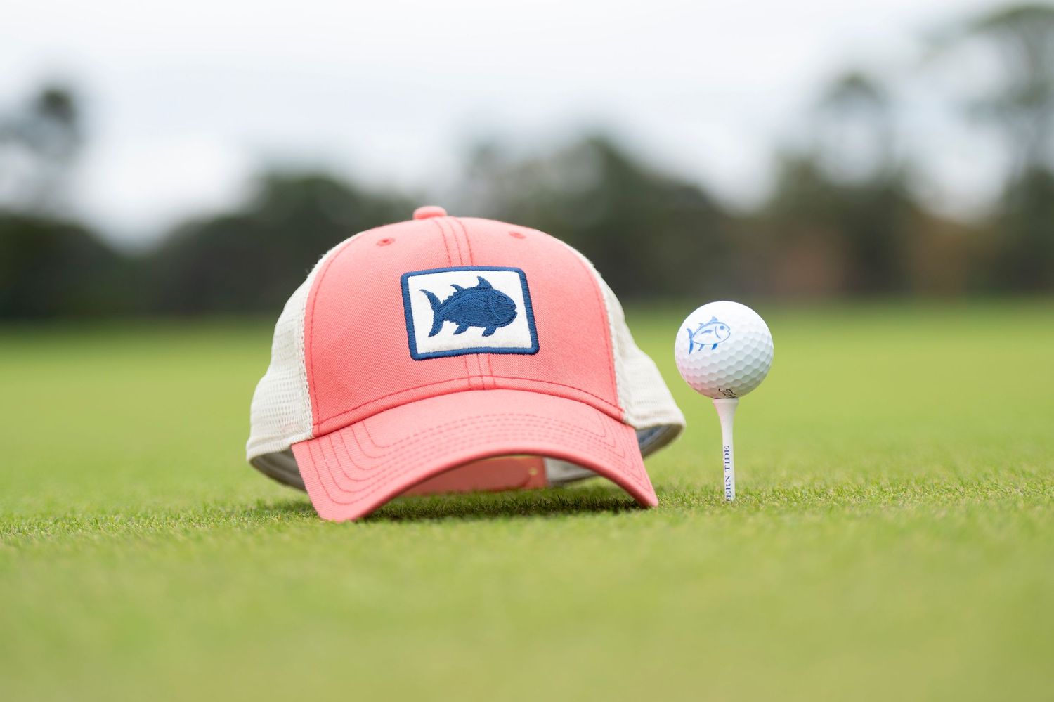 Coral Southern Tide hat and golf ball staged on golf course grass.