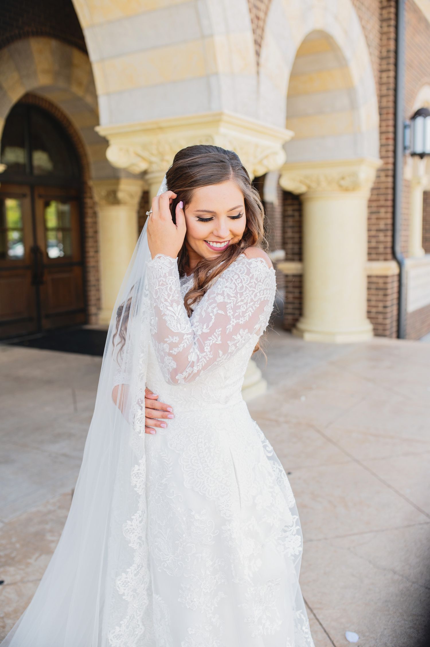 A bride in a lace wedding dress and veil poses in an elegant arched colonnade during a bridal photo session.