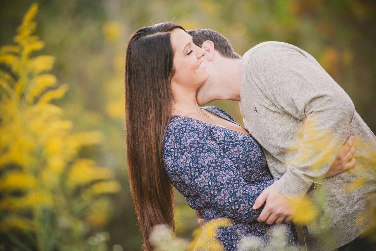 Engagement session Couple embracing in autumn garden with yellow flowers in background.