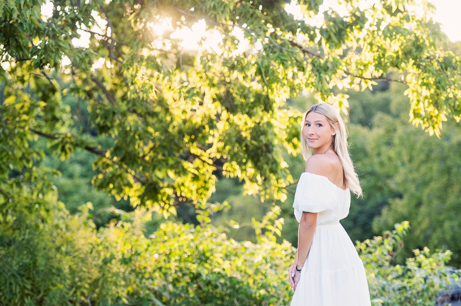 Sunset portrait in white dress against golden backlit trees.