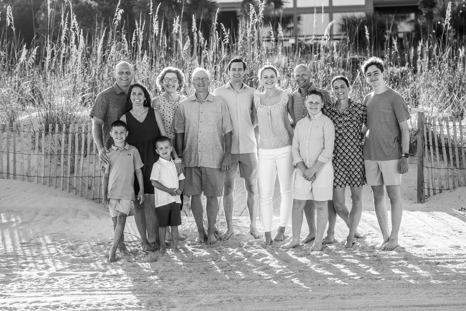 Black and white beach portrait of family members standing together near coastal vegetation.