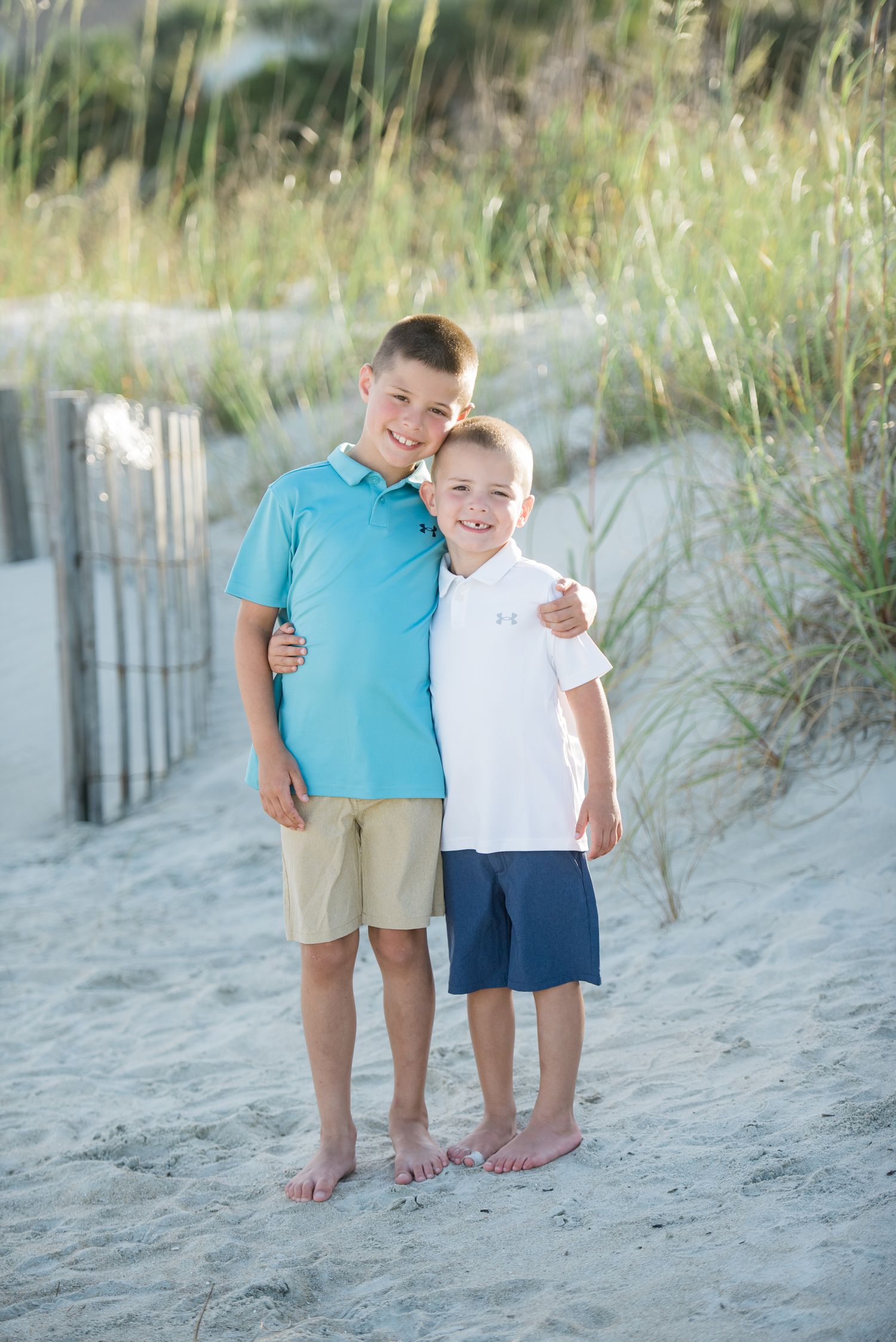 Two children sharing a sweet moment together on a sandy beach path with coastal vegetation. Sea Pines