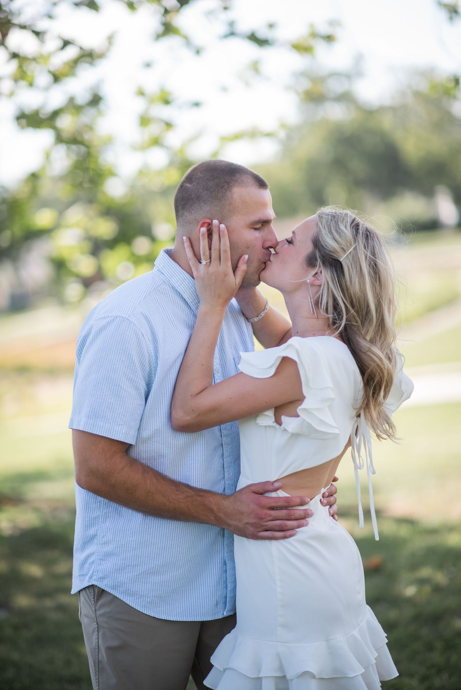A romantic couple shares tender kisses in an outdoor setting wearing coordinated light blue and white outfits.