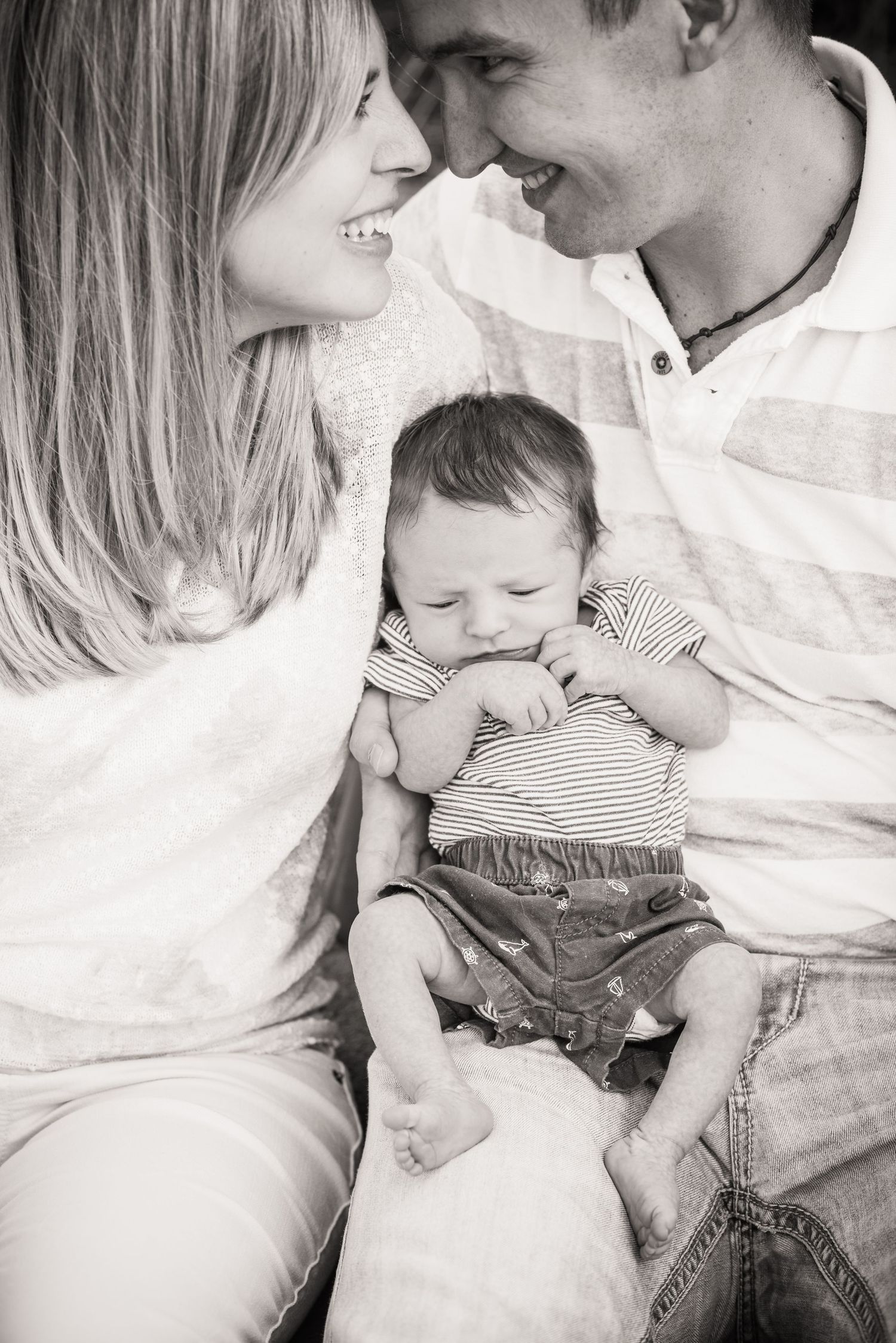 Black and white family portrait with baby between parents sharing tender moments.
