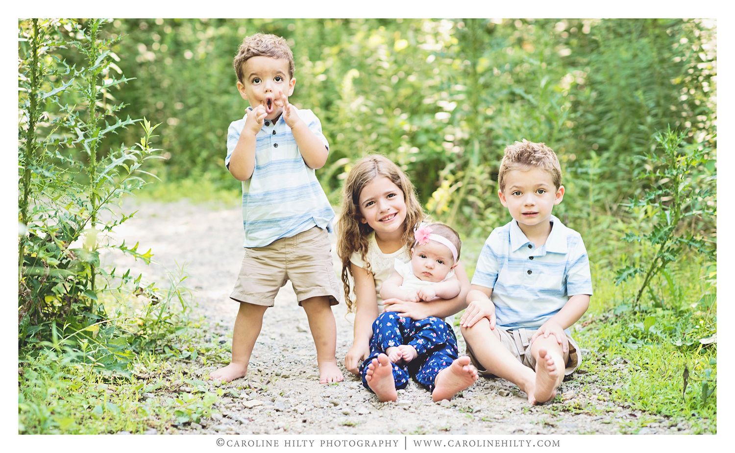 Children play and explore together on a gravel path surrounded by lush green foliage on a sunny summer day.