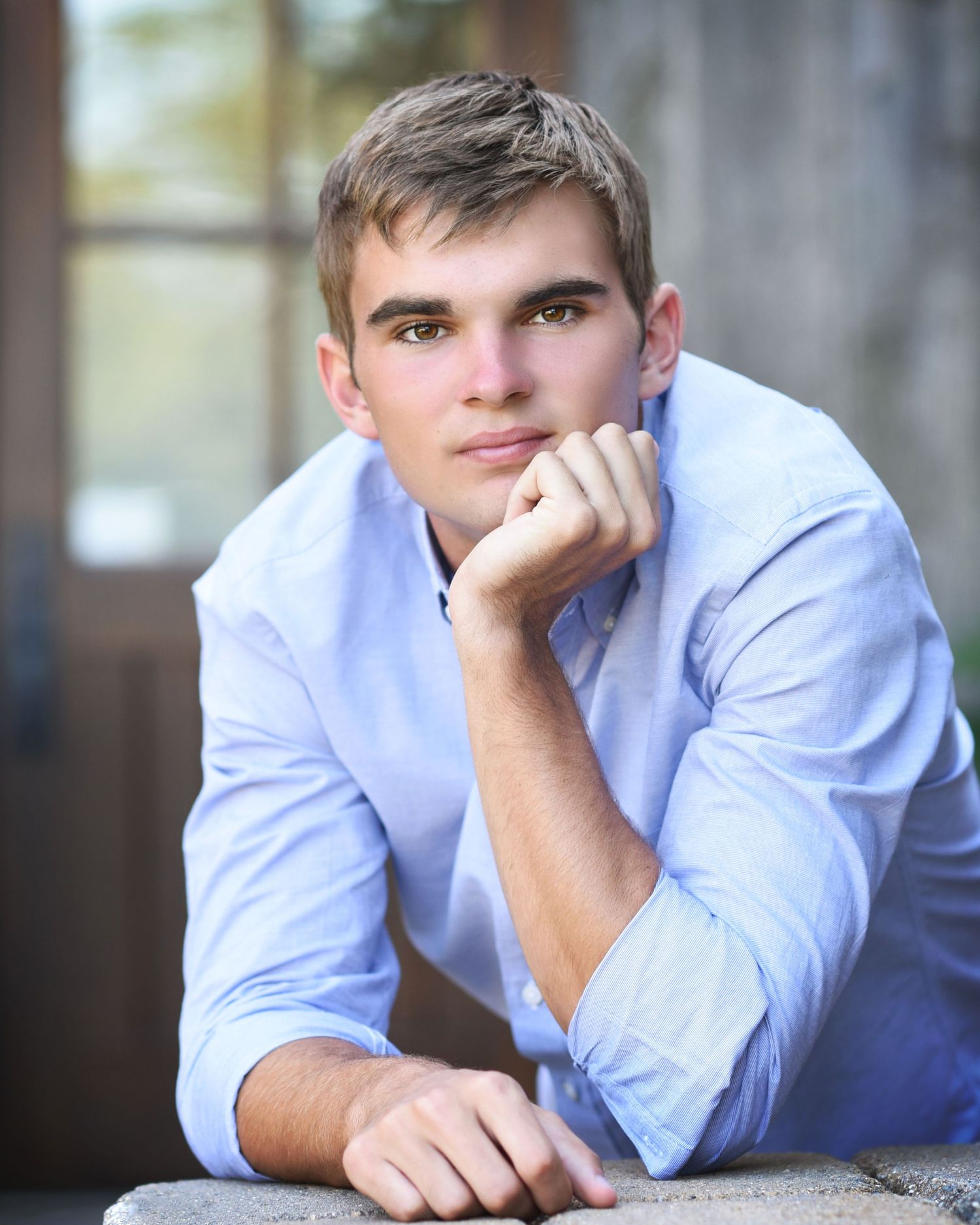 Person in light blue button-down shirt rests on concrete surface during outdoor portrait session.