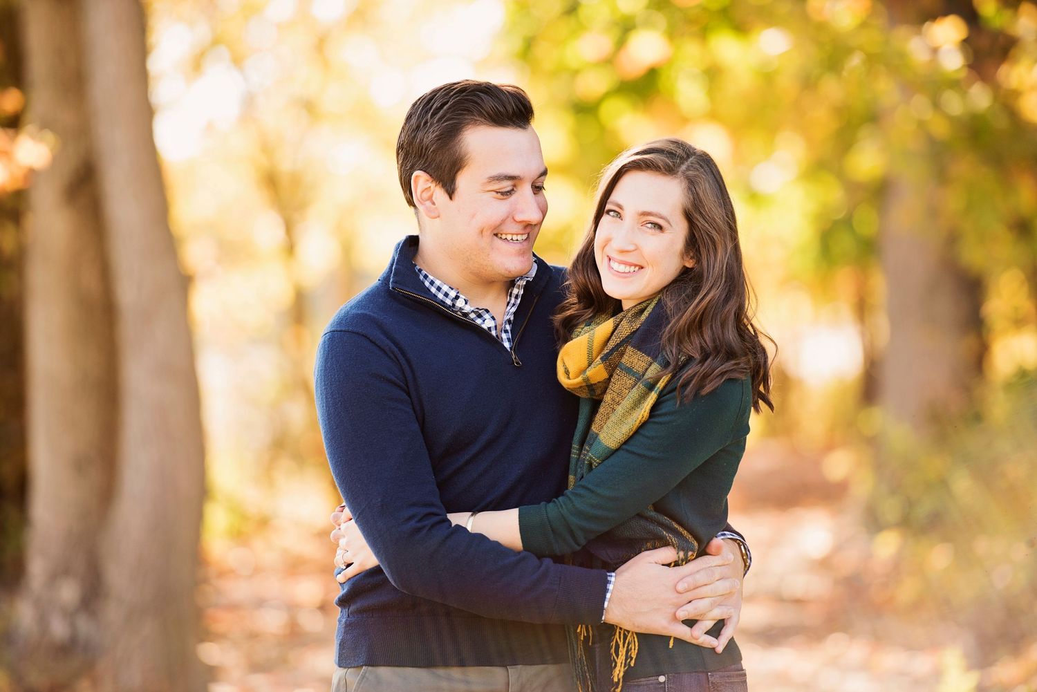 A couple shares romantic moments in an autumn setting with golden sunlight filtering through trees in the background.