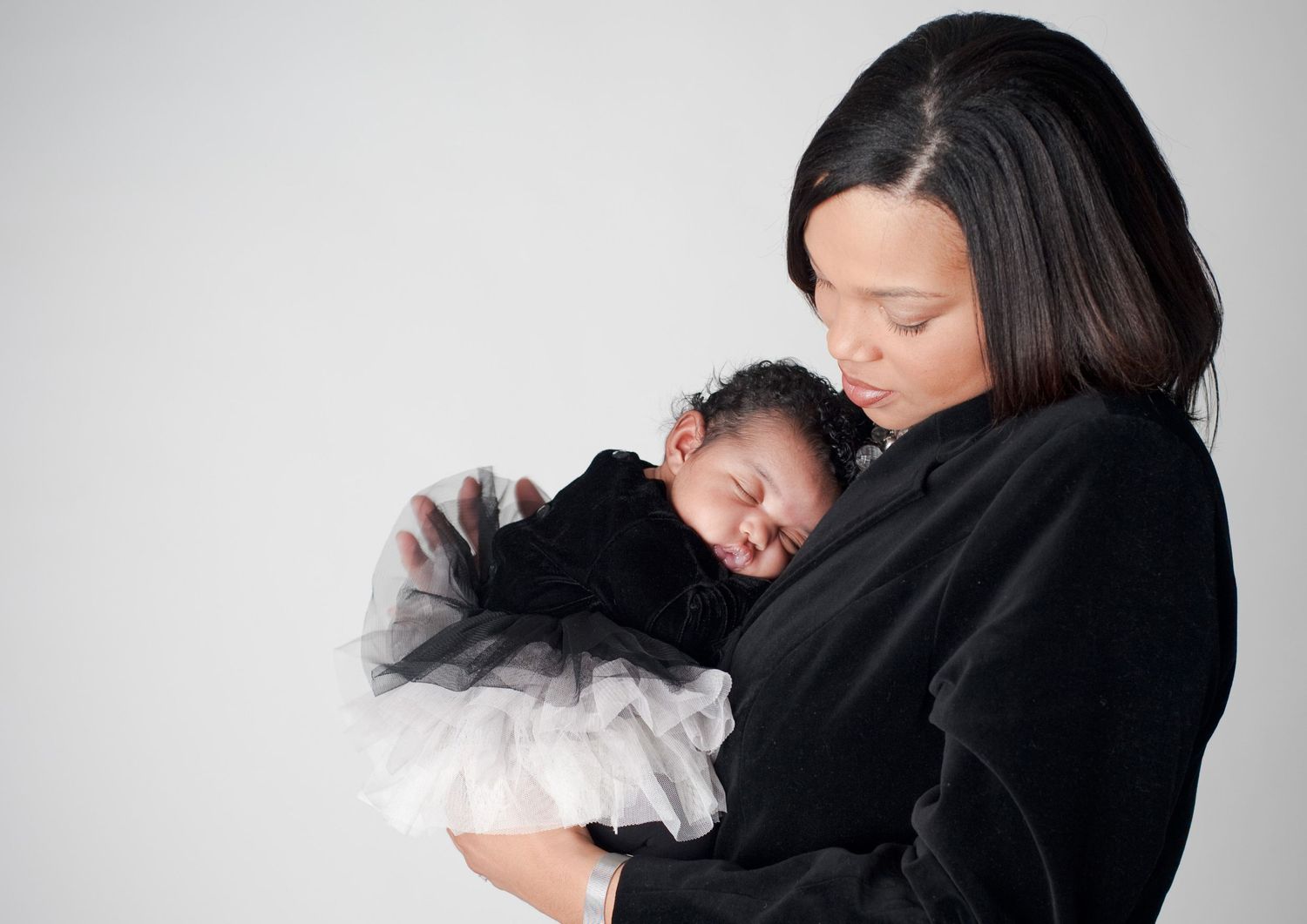 A tender moment between mother and newborn baby as they embrace against a light background.