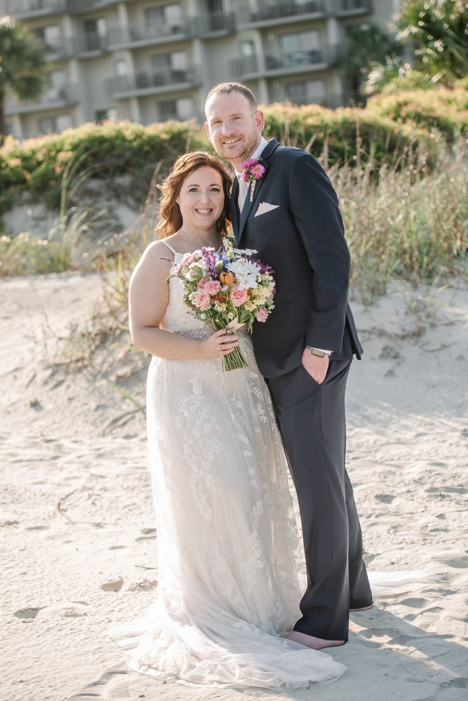 Couple shares intimate moments during their beach wedding photoshoot near coastal buildings.