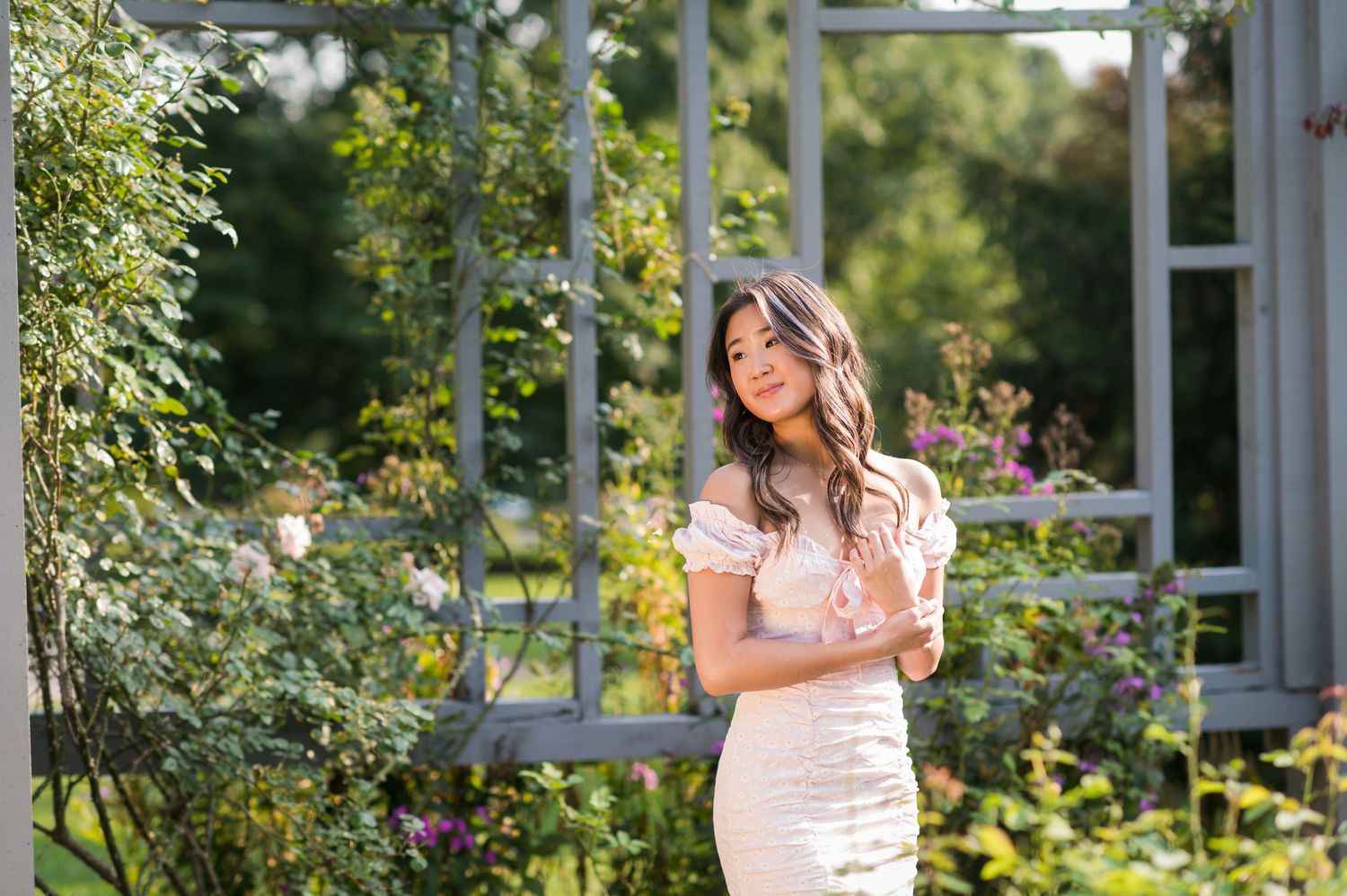 A person stands in a lush garden setting with blooming flowers and greenery on a sunny summer day.