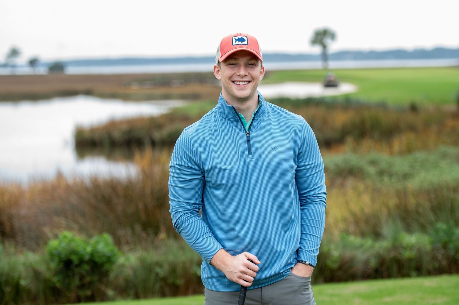 Golfer in light blue polo shirt poses against coastal marsh landscape background. Southern Tide Brand editorial photoshoot.