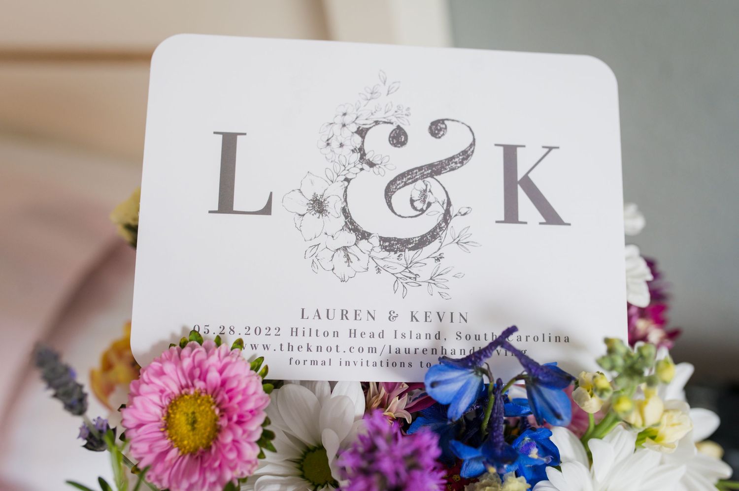 Wedding monogram design with decorative floral elements displayed on white cards surrounded by pink and purple flowers.