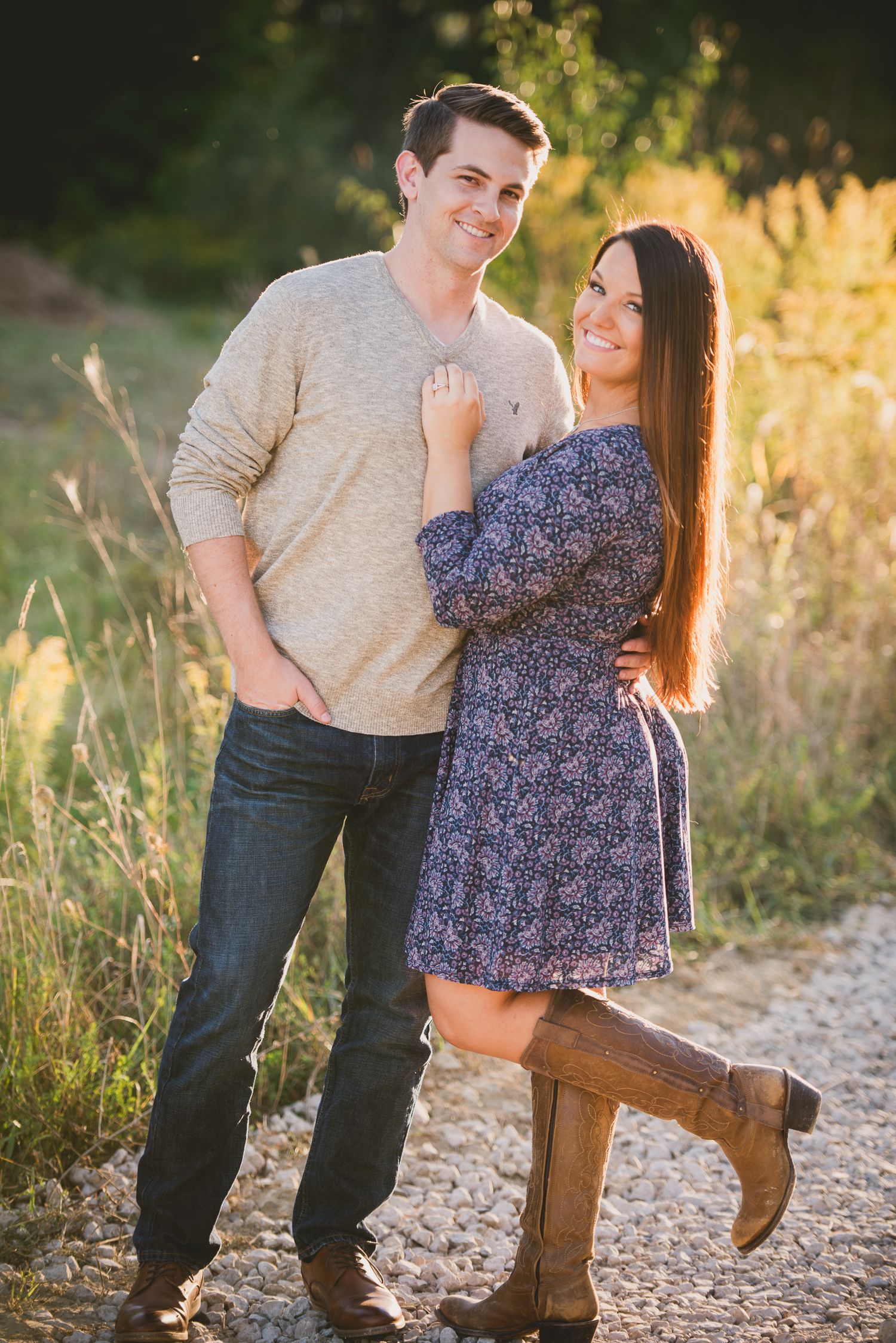 Romantic couple in casual attire share intimate moments on a gravel path during golden hour sunset.
