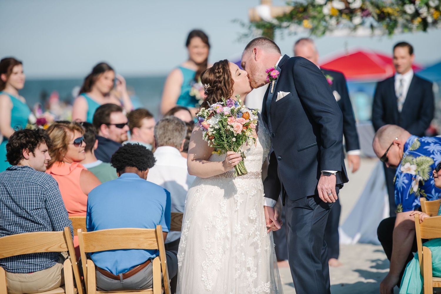 Beach wedding ceremony setup with wooden chairs and floral arch overlooking the ocean.