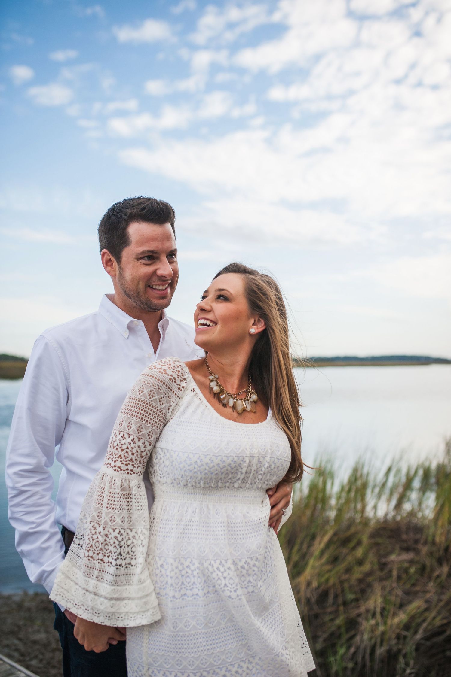 Couple shares intimate moment by marsh landscape wearing coordinated white and navy outfits.