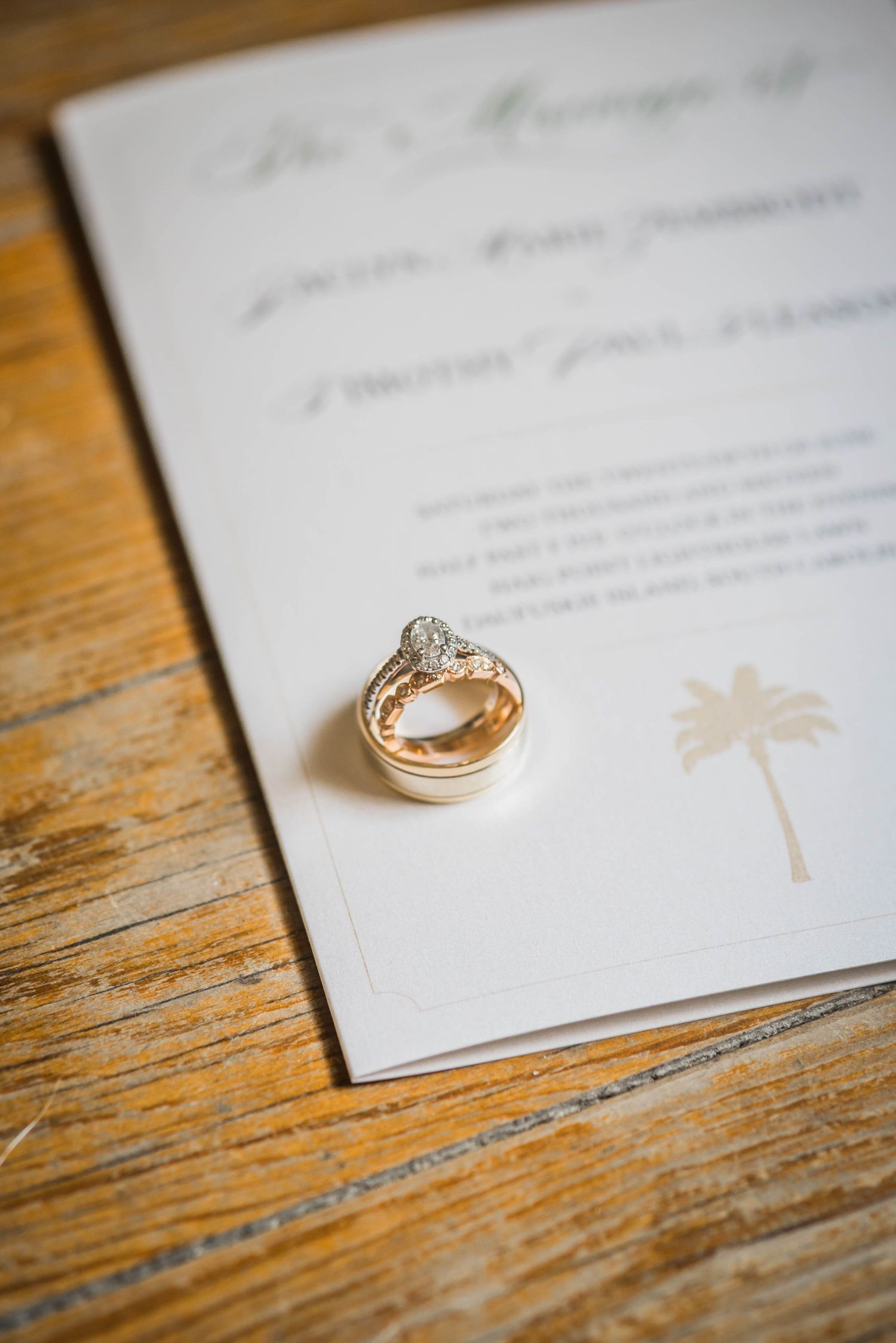 Wedding rings rest on a white invitation card against rustic wooden table surface, creating an elegant composition.