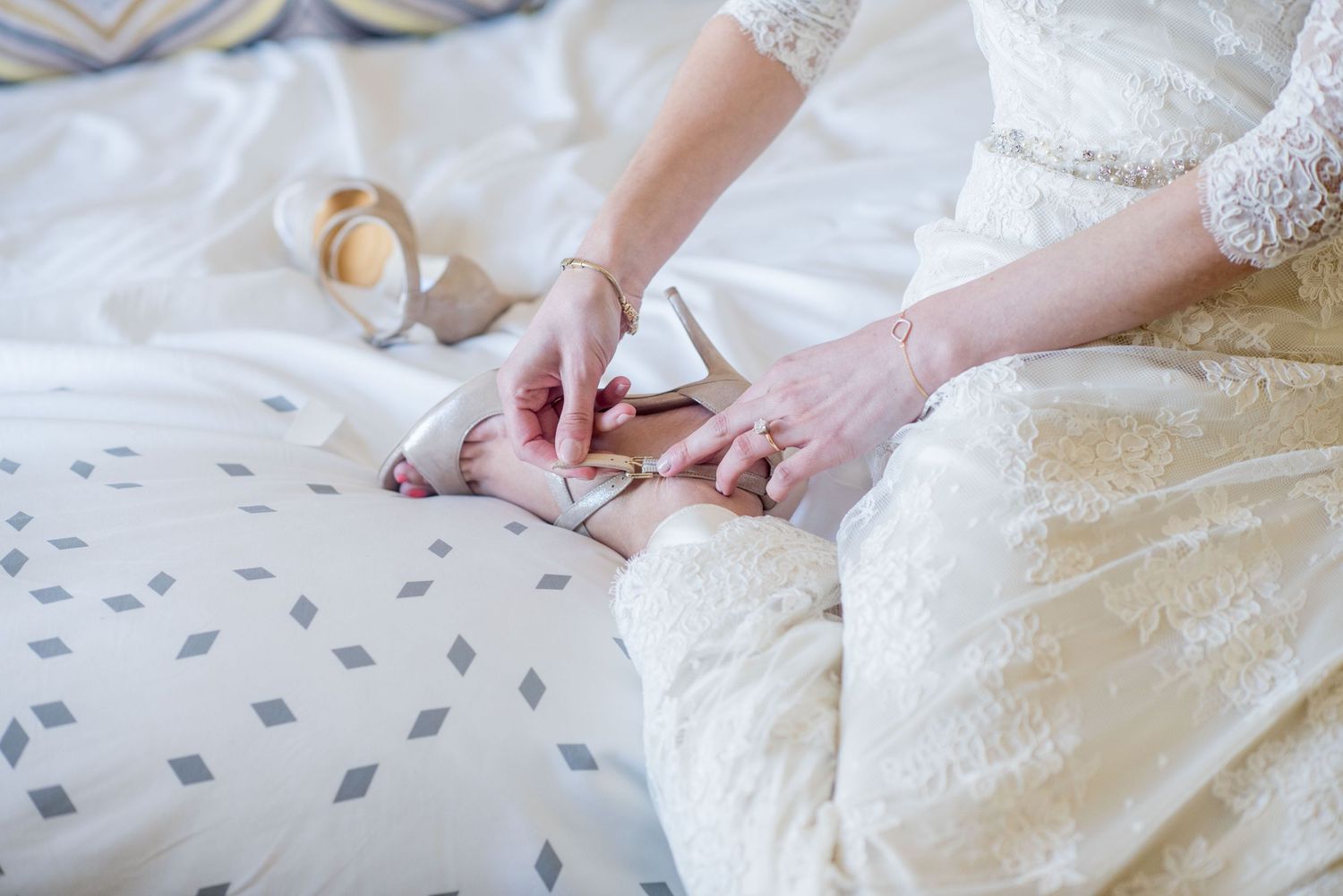Close-up view of hands sewing delicate beadwork and lace details onto white wedding dress fabric.
