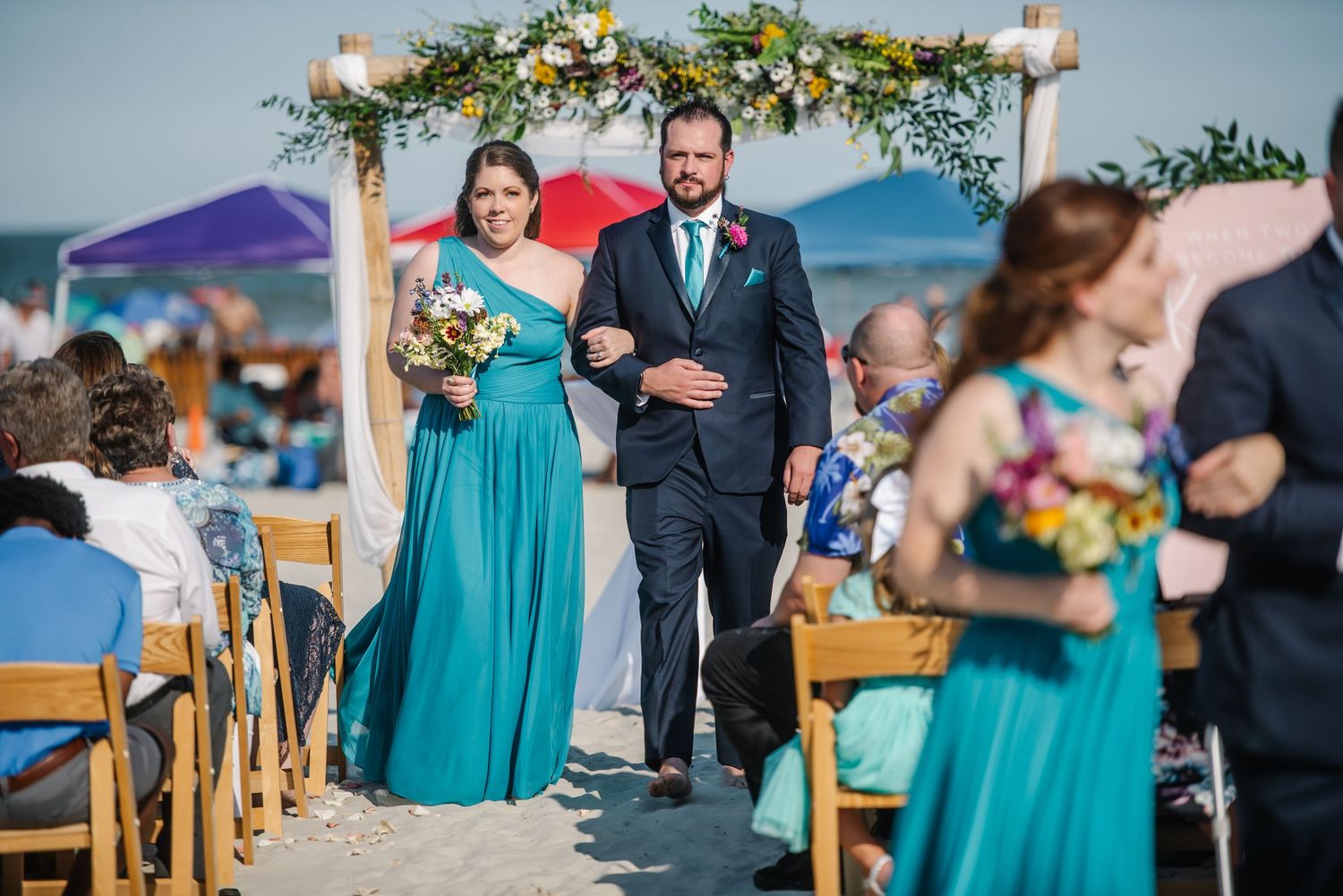Outdoor beach wedding ceremony with turquoise bridesmaid dresses and floral decorations.