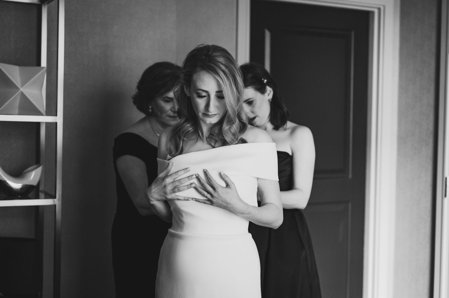 A tender moment captured in black and white as bridesmaids help adjust a wedding dress.