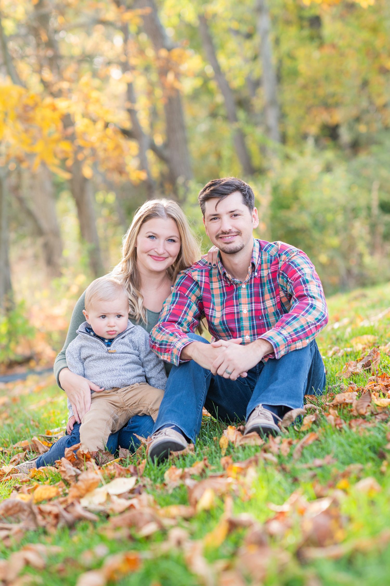 A family sits together on fallen autumn leaves during a fall outdoor photo session.