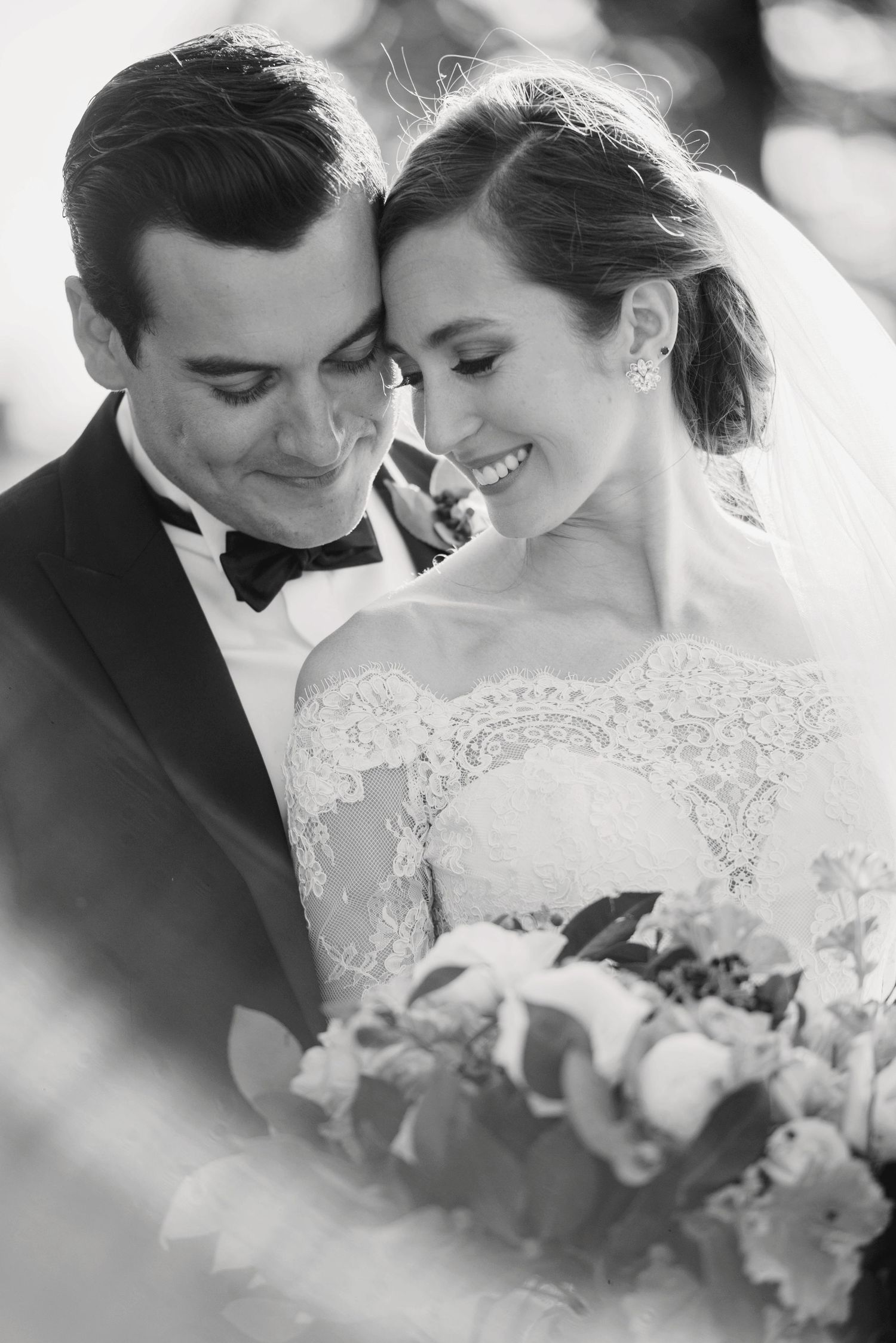 A black and white intimate wedding portrait showing a couple with lace dress details.