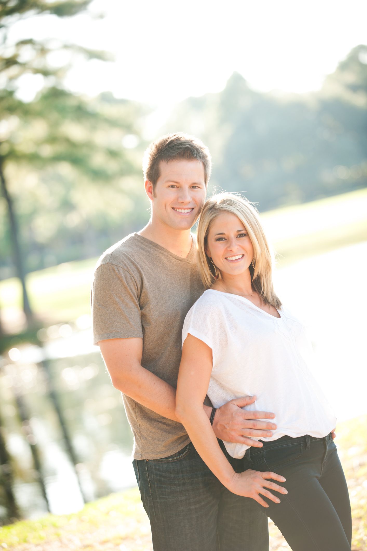 A couple embraces in warm sunlight during an outdoor photo session with a natural scenic background.
