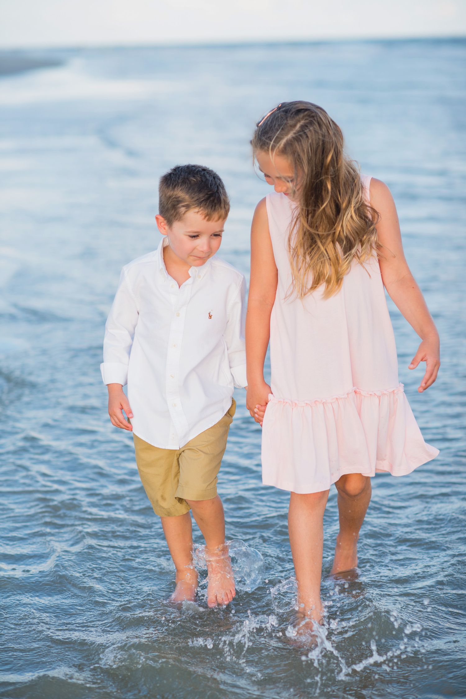 Children splashing and playing in ocean waves wearing coordinated white and pink outfits. St. Augustine Beach, Hammock Beach photographer.