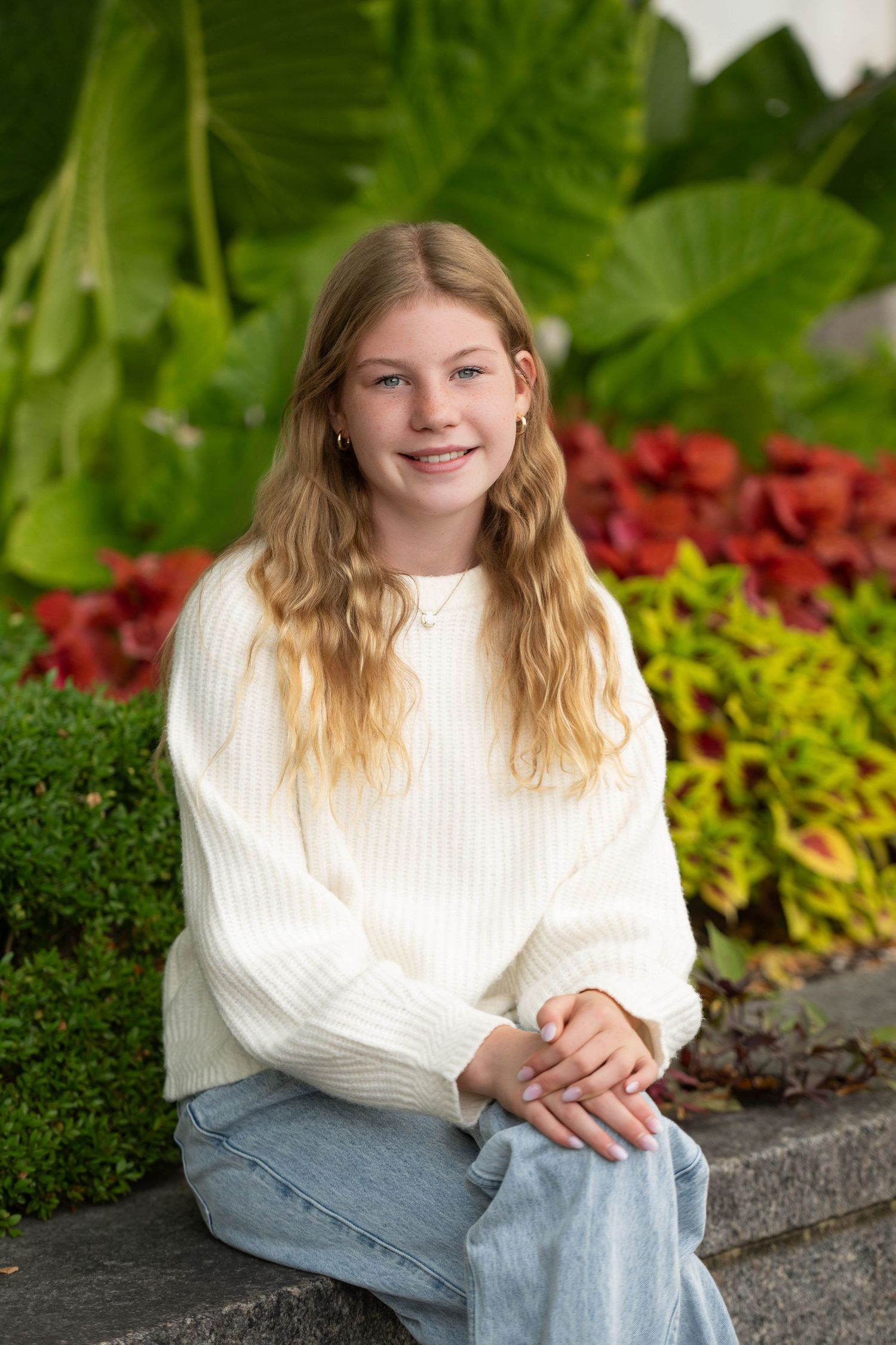 A series of outdoor portraits featuring someone in a white sweater and jeans sitting on a stone wall with colorful plants behind.