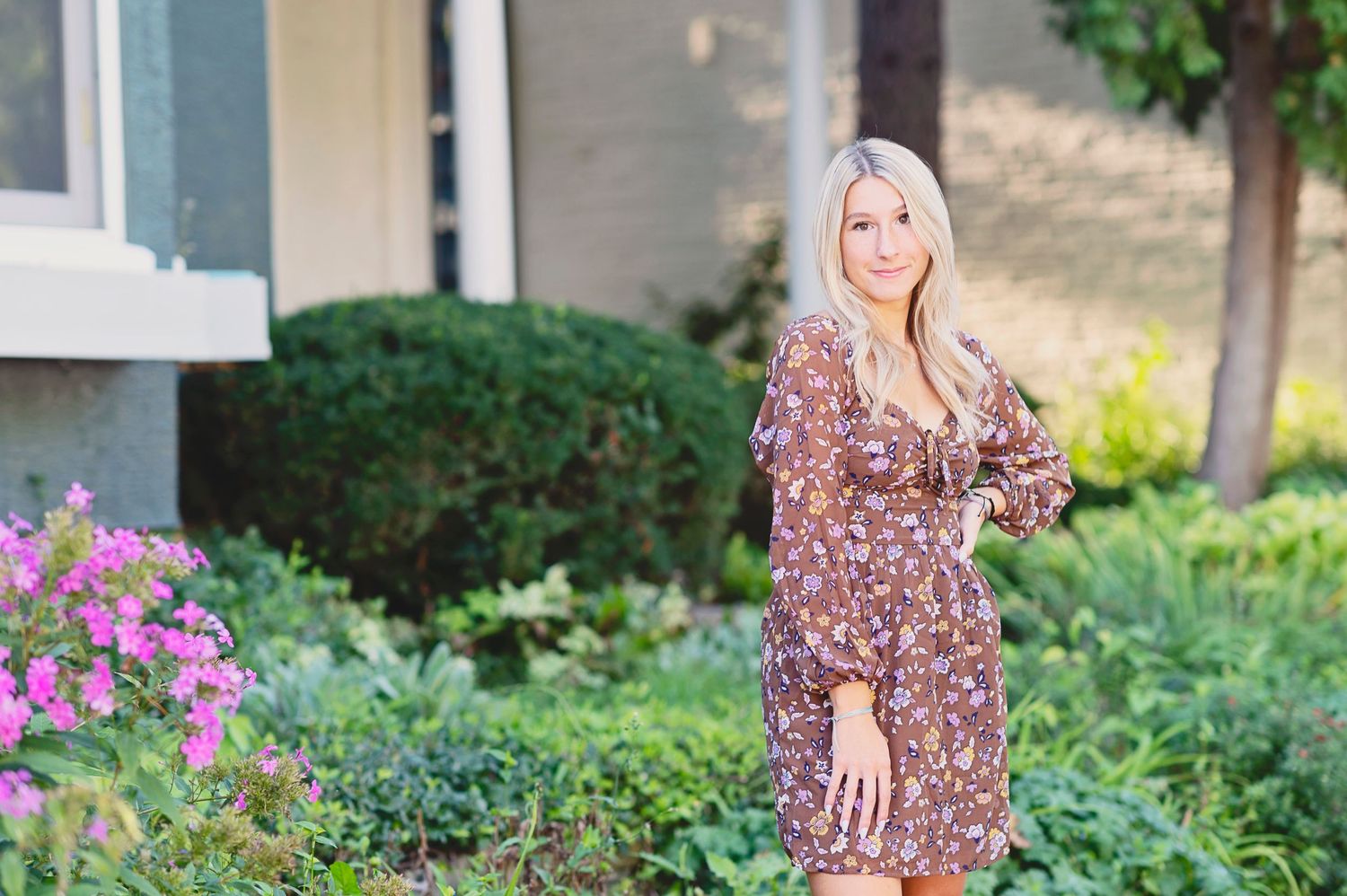 A floral print dress worn in a garden setting with pink flowers and greenery in the background.