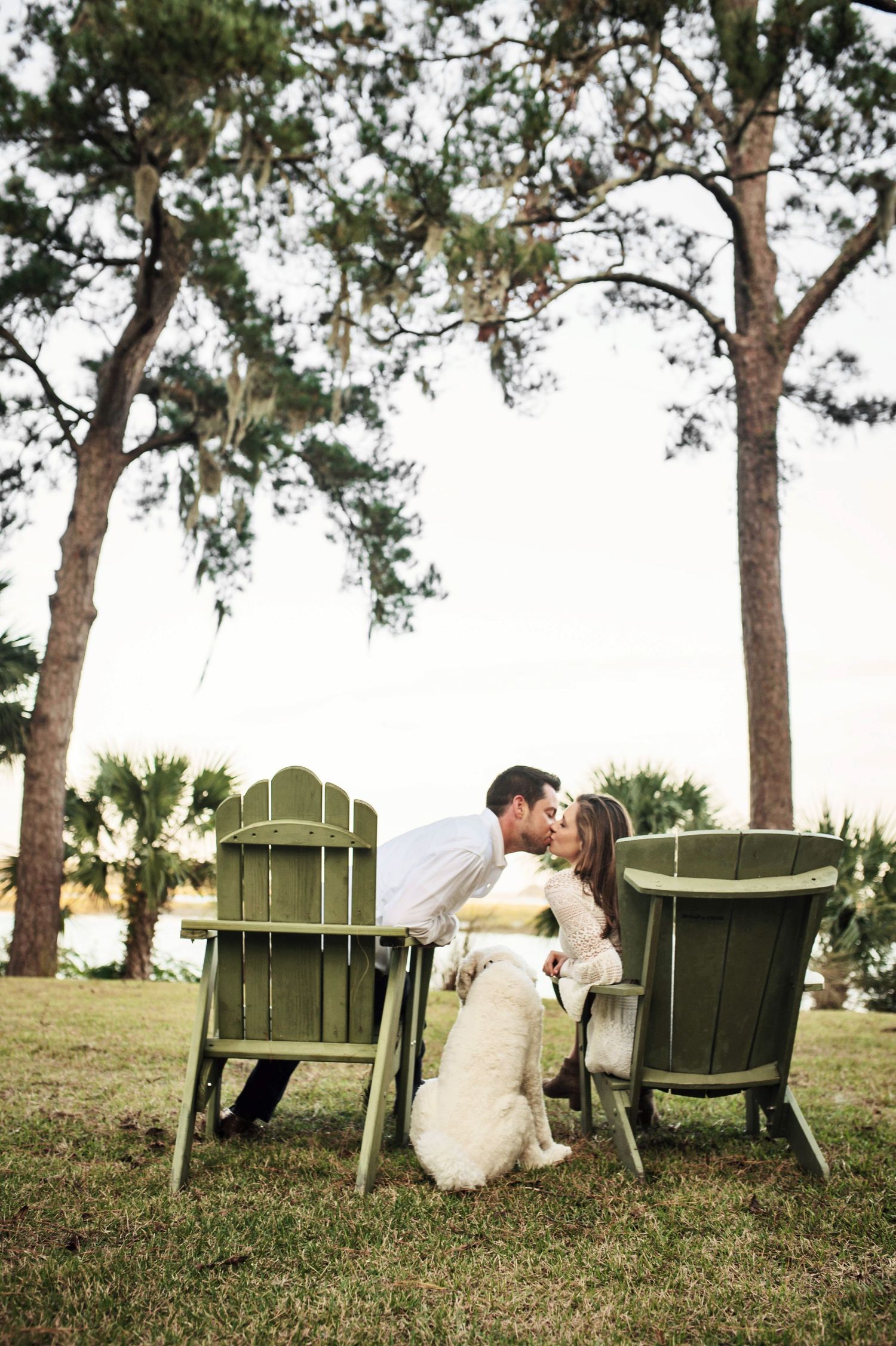 Green Adirondack chairs set up on grassy hill under pine trees for romantic outdoor portraits.