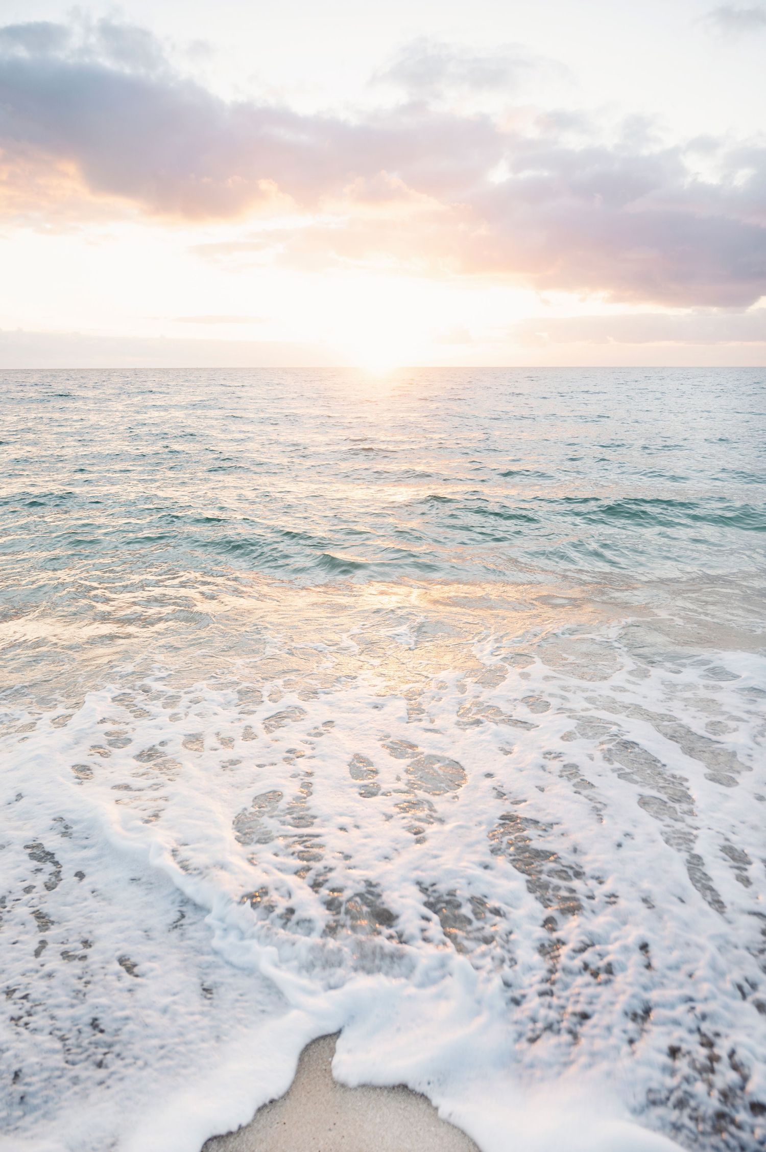 Florida Ocean waves crash onto shore during a pastel sunset with soft clouds reflecting pink and orange hues on the water.