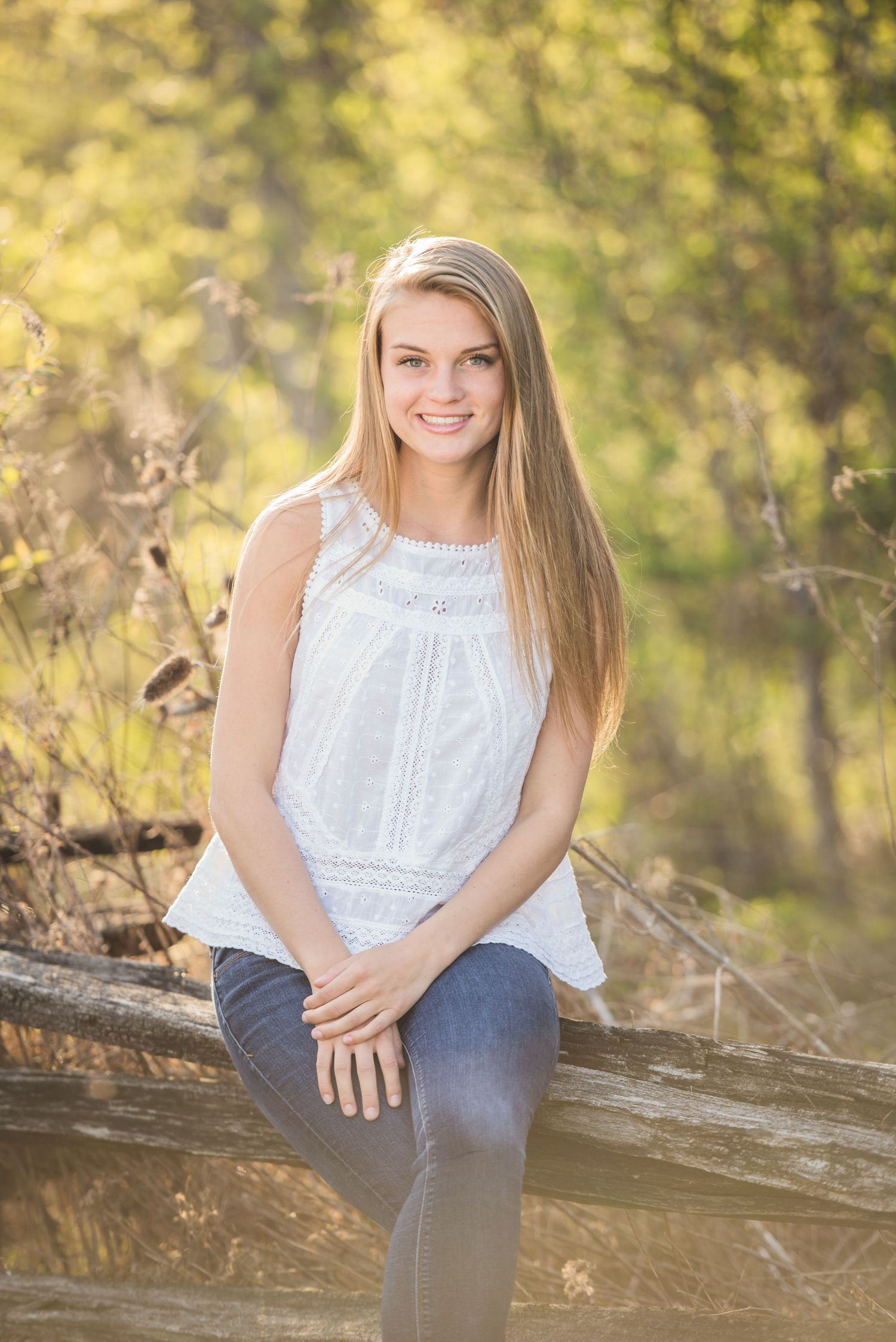 Spring portrait session featuring white eyelet top and casual pose on weathered wood.