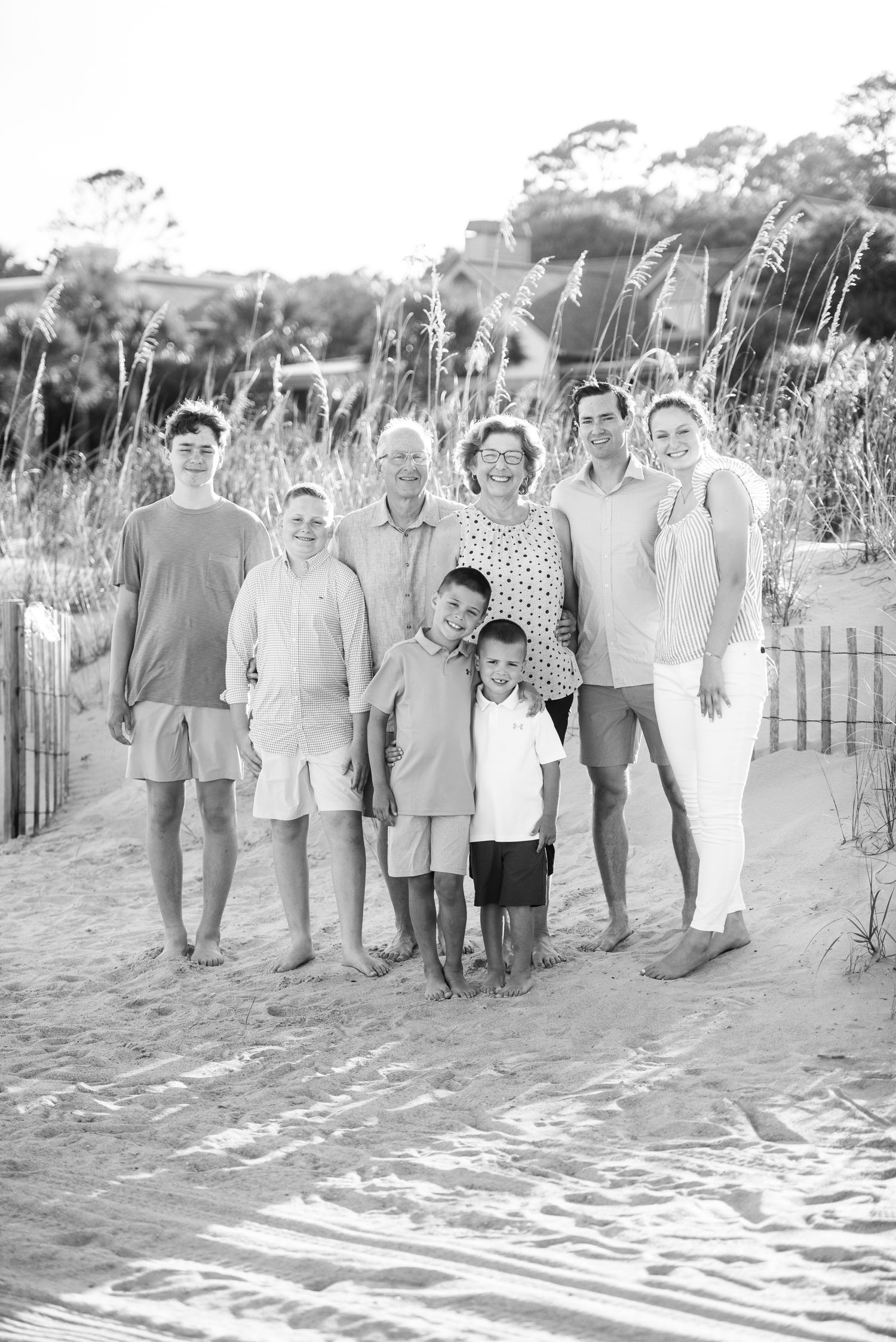 Black and white group photo of extended family lined up on beach sand with sea oats. Sea Pines