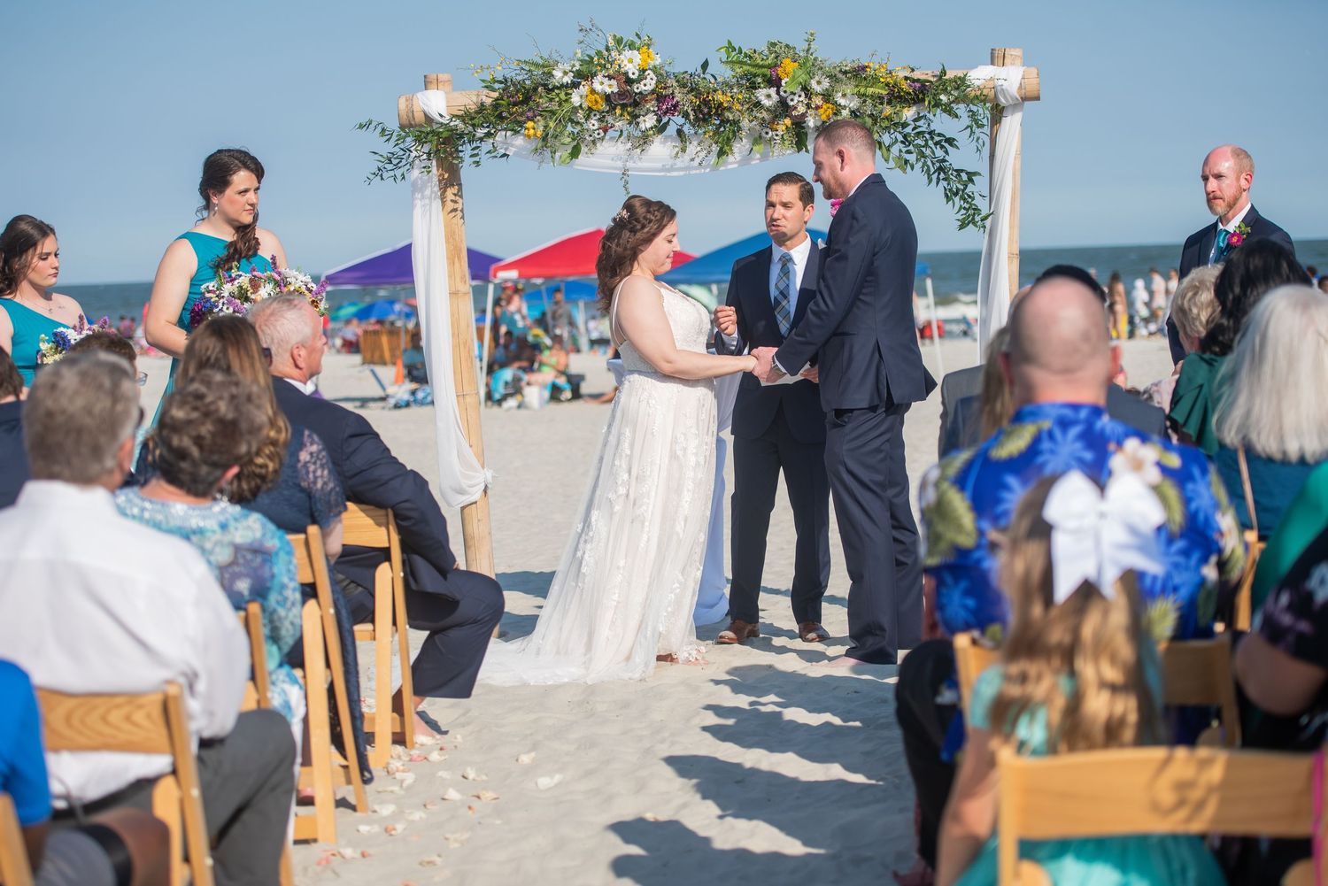 Beachfront wedding ceremony setup with wooden chairs and floral arch against ocean backdrop. Beach House Hilton Head