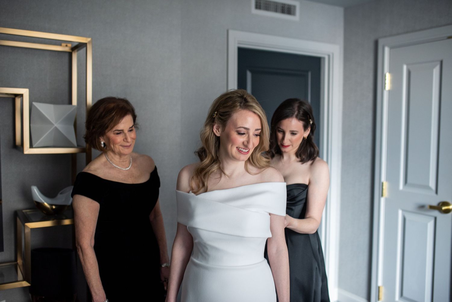 Wedding preparation scene with women in formal attire getting ready in an elegant room.