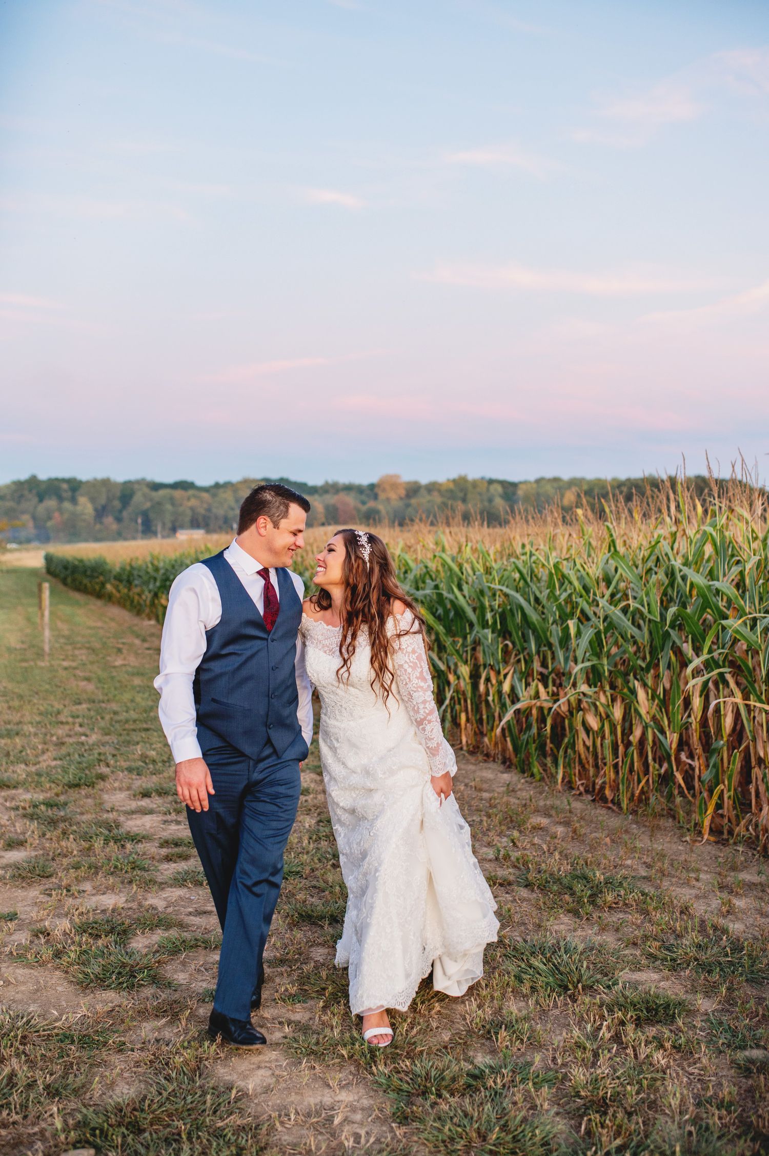 A couple shares a romantic moment at sunset beside a cornfield on their wedding day.