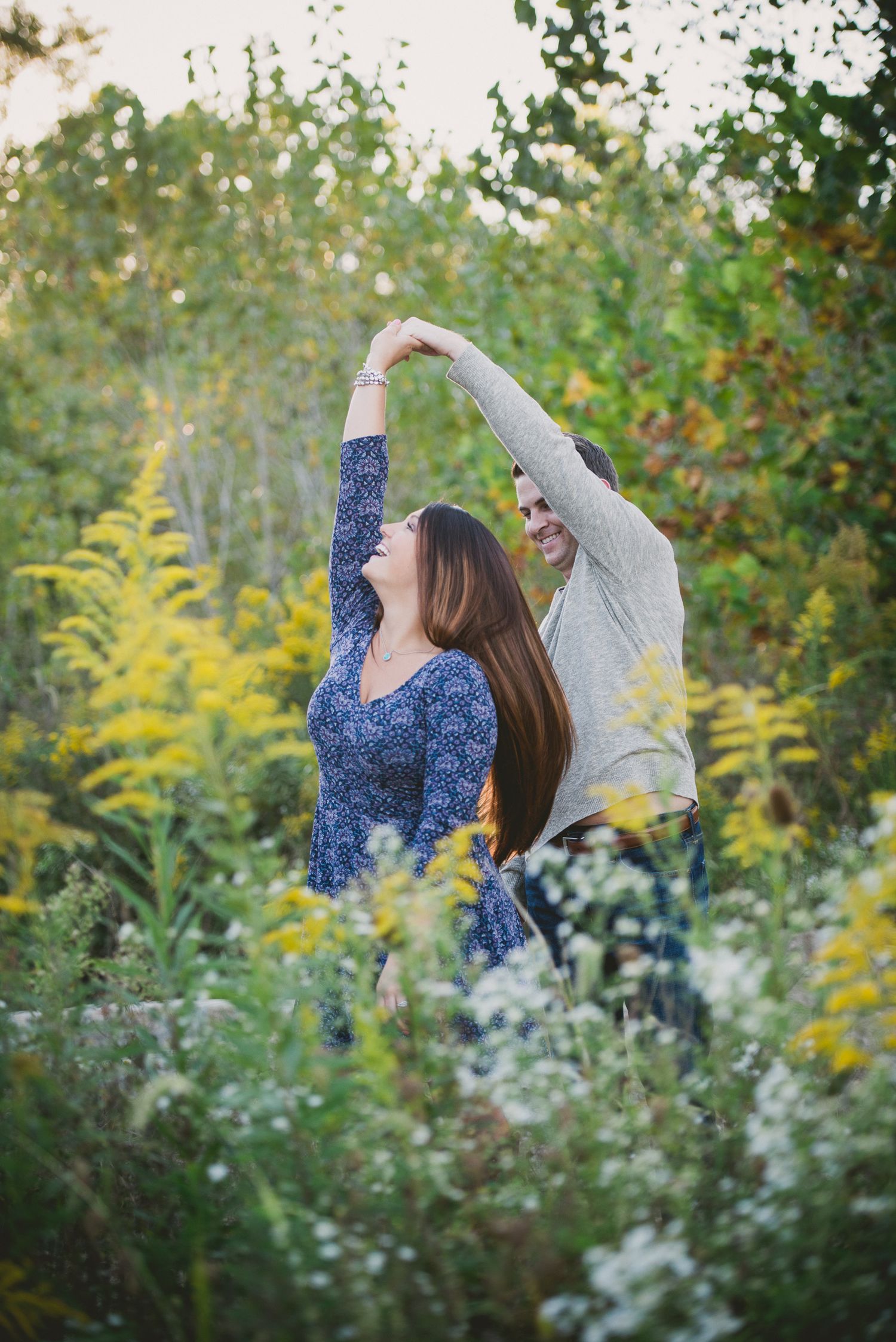 engaged Couple dancing together in garden with white and yellow wildflowers.