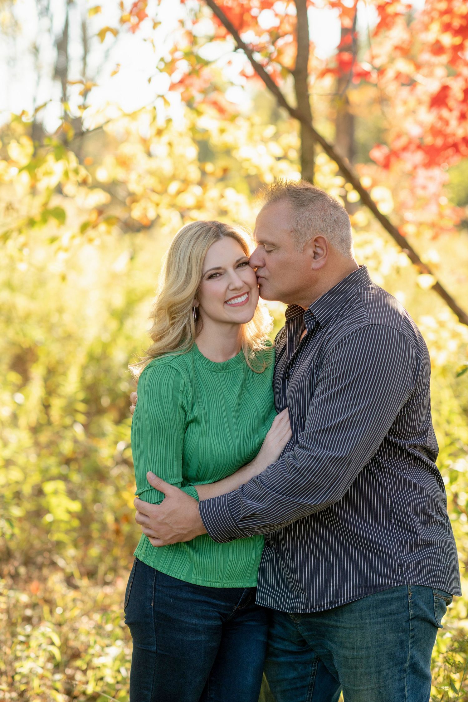 Romantic autumn photoshoot with couple in green and grey outfits against colorful fall foliage.