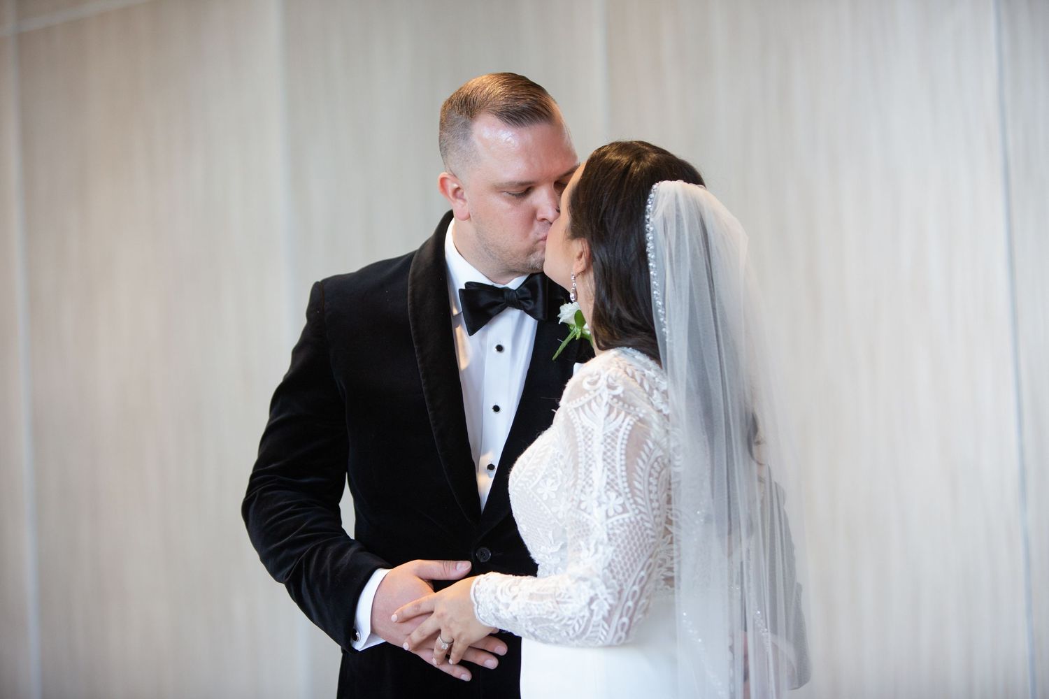 A tender moment between newlyweds as they embrace, with the bride in white lace and groom in classic black tuxedo.