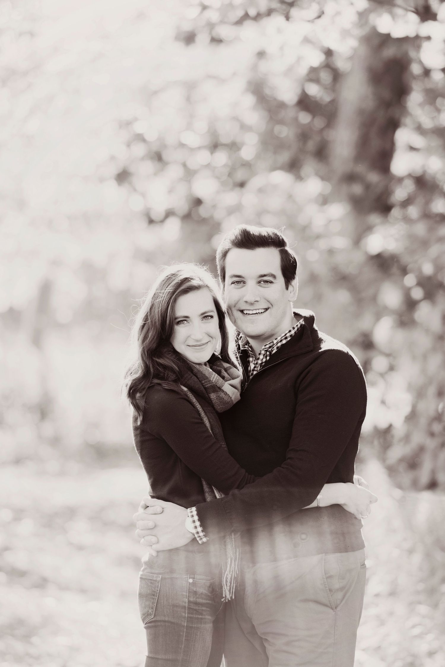 A couple embraces and smiles outdoors in a series of black and white romantic engagement photos.